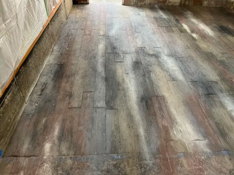 Wooden plank floor in a room, with gray-brown weathered boards and a white wall on the left.