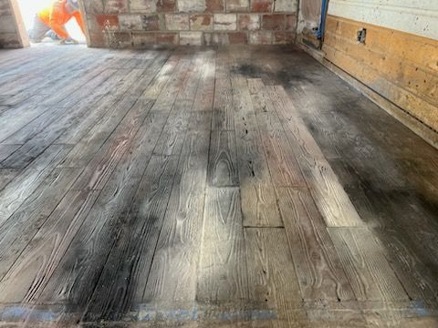 Weathered wooden floor inside a room with a brick wall and orange tarp in the corner.