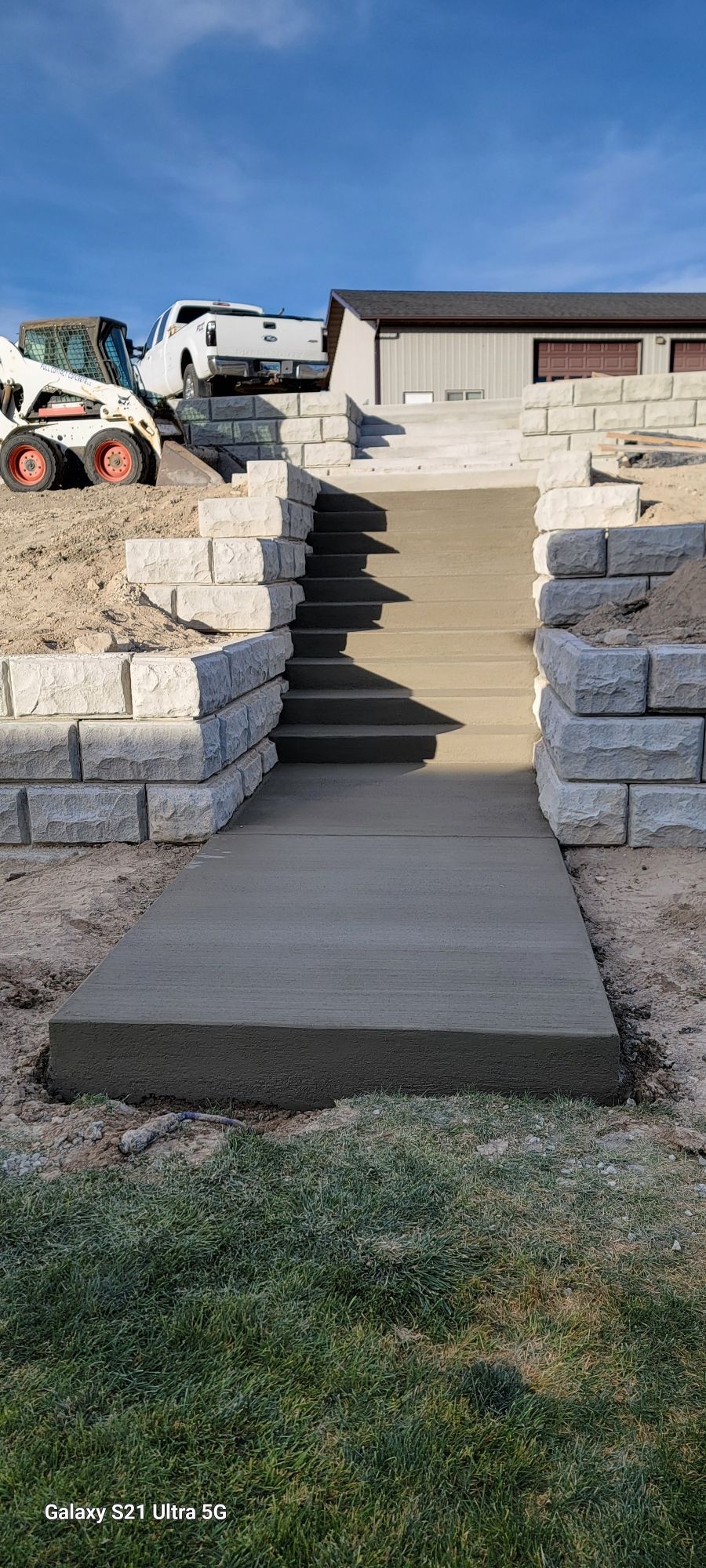 Concrete ramp and steps leading up a stone retaining wall beside a house under construction.