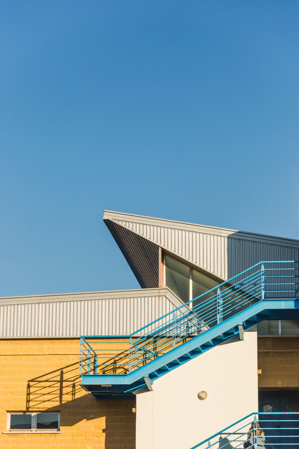 Blue staircase with turquoise railings on a tan building under a clear sky