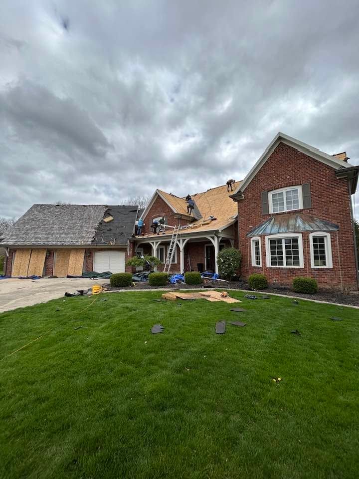 Brick house with large front lawn, cloudy sky, and a detached garage with exposed framing.