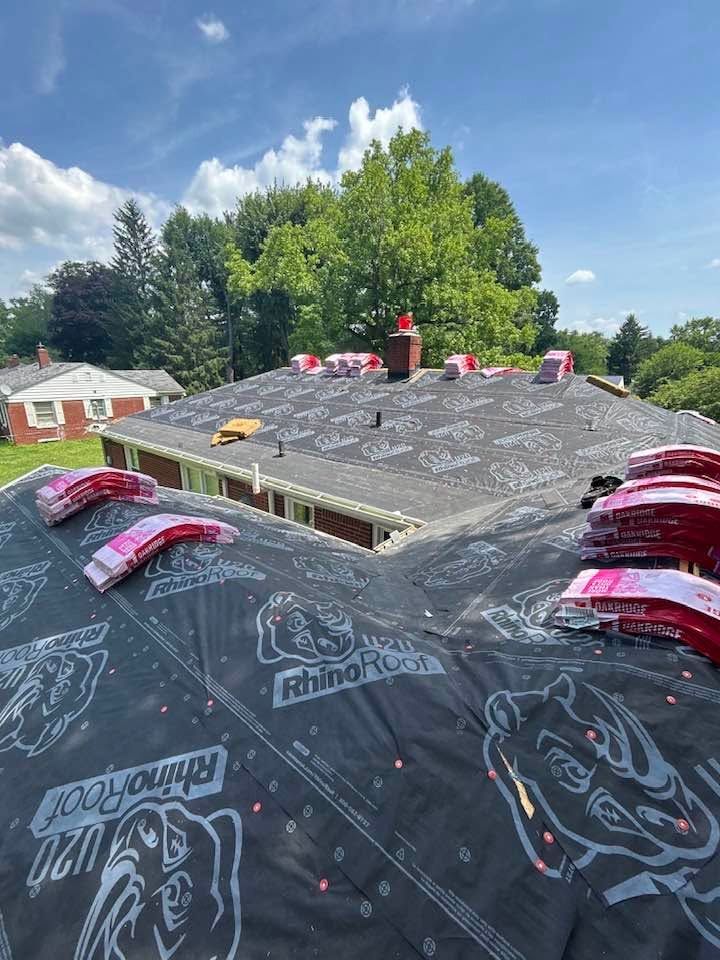 Roof under repair with black underlayment and red roofing materials on a house under a partly cloudy sky
