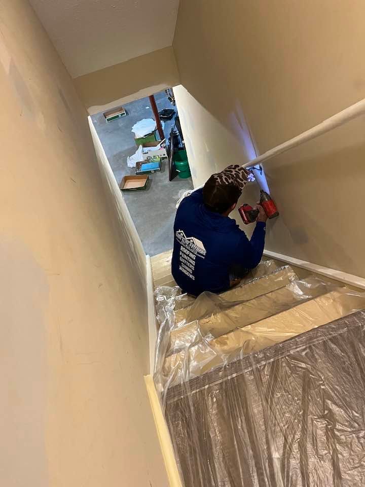 Person kneeling on a stairway, installing the railing near a plastic-covered floor during home renovation