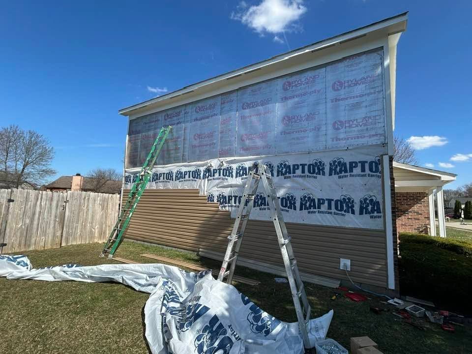 House under construction with house wrap, ladders, and scaffolding against a blue sky