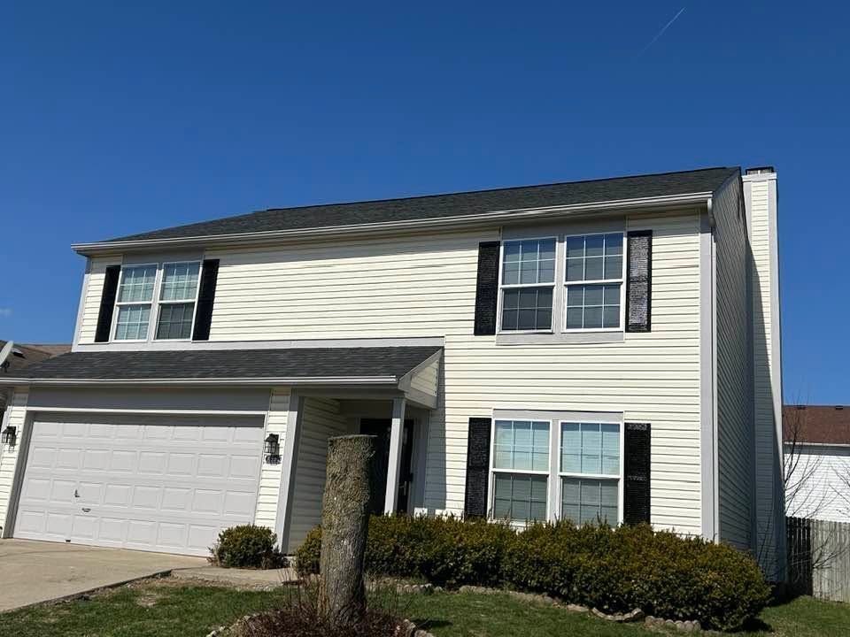Suburban two-story house with white siding, gray roof, attached garage, and trimmed bushes under a clear blue sky