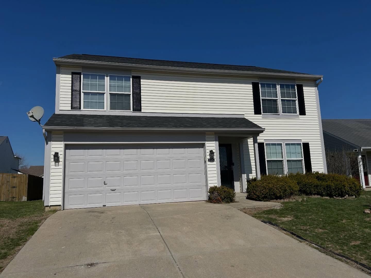 Two-story suburban house with white siding, a two-car garage, and a concrete driveway under a blue sky.