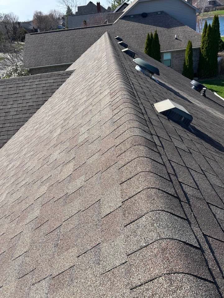 Gable roof with gray shingles and several rooftop vents in a residential neighborhood.