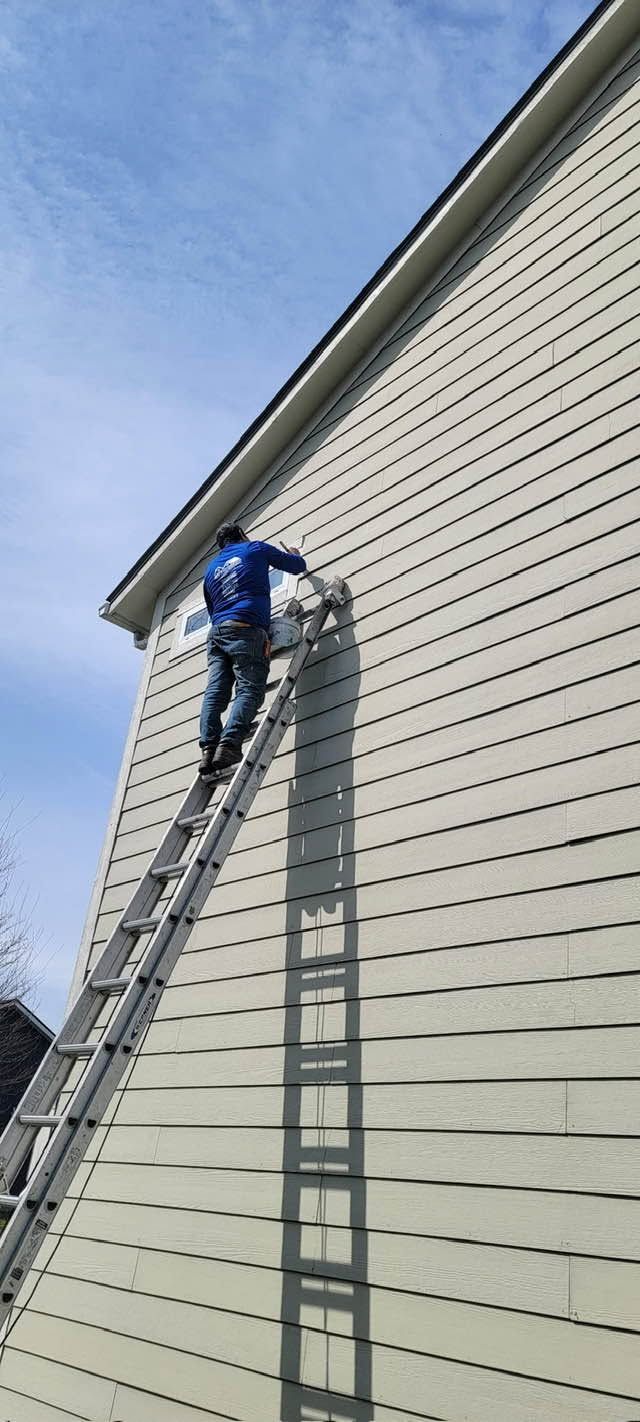 Worker on a ladder working on beige siding on a home