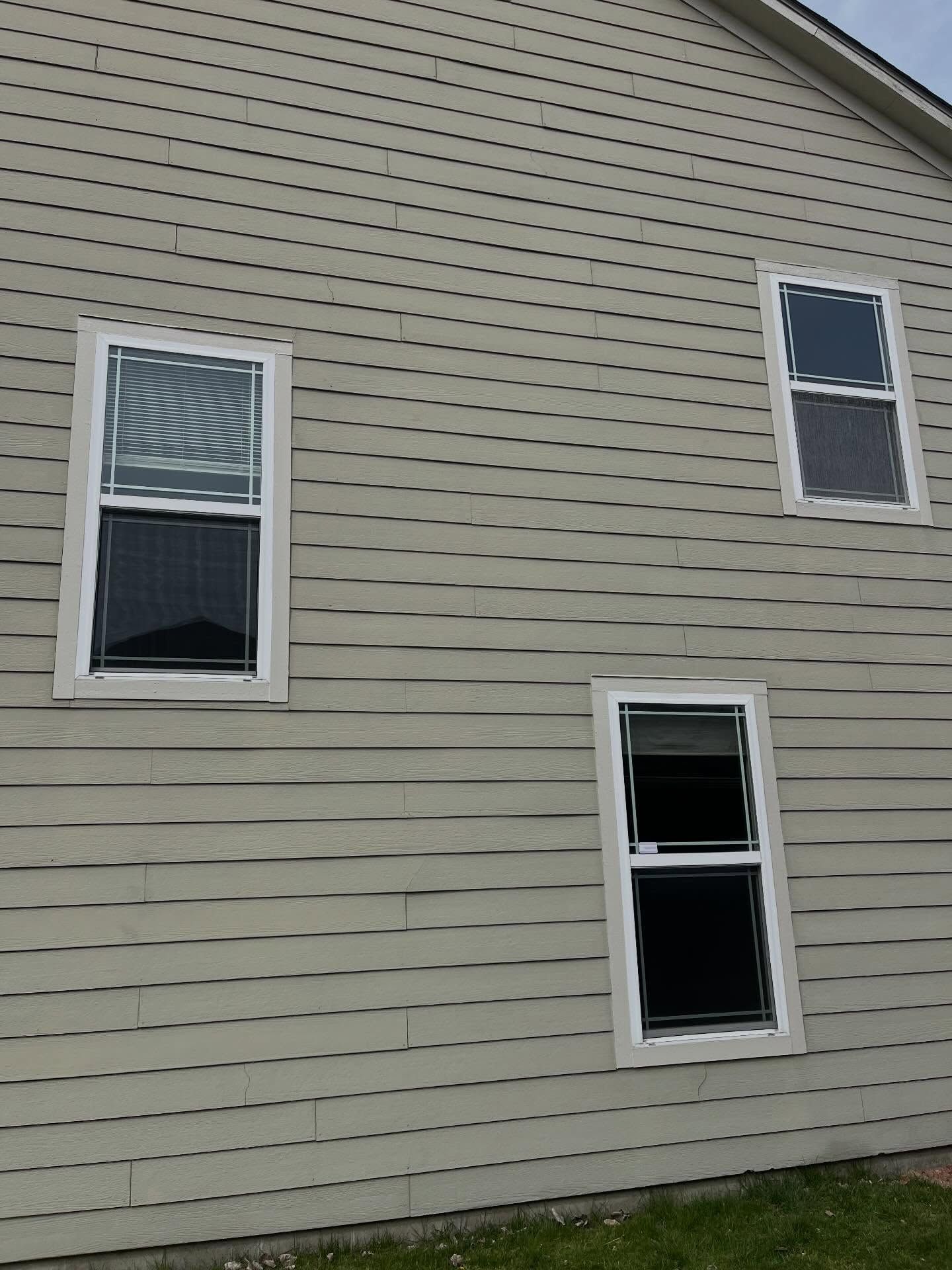 Side of a beige house with three white-trimmed windows on horizontal siding