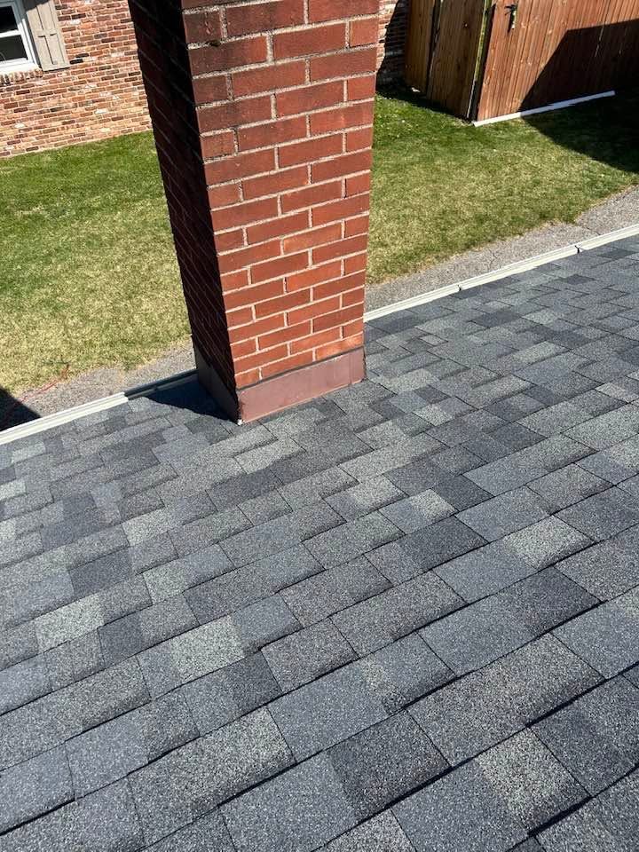 Brick chimney beside gray shingles and a green lawn in bright sunlight