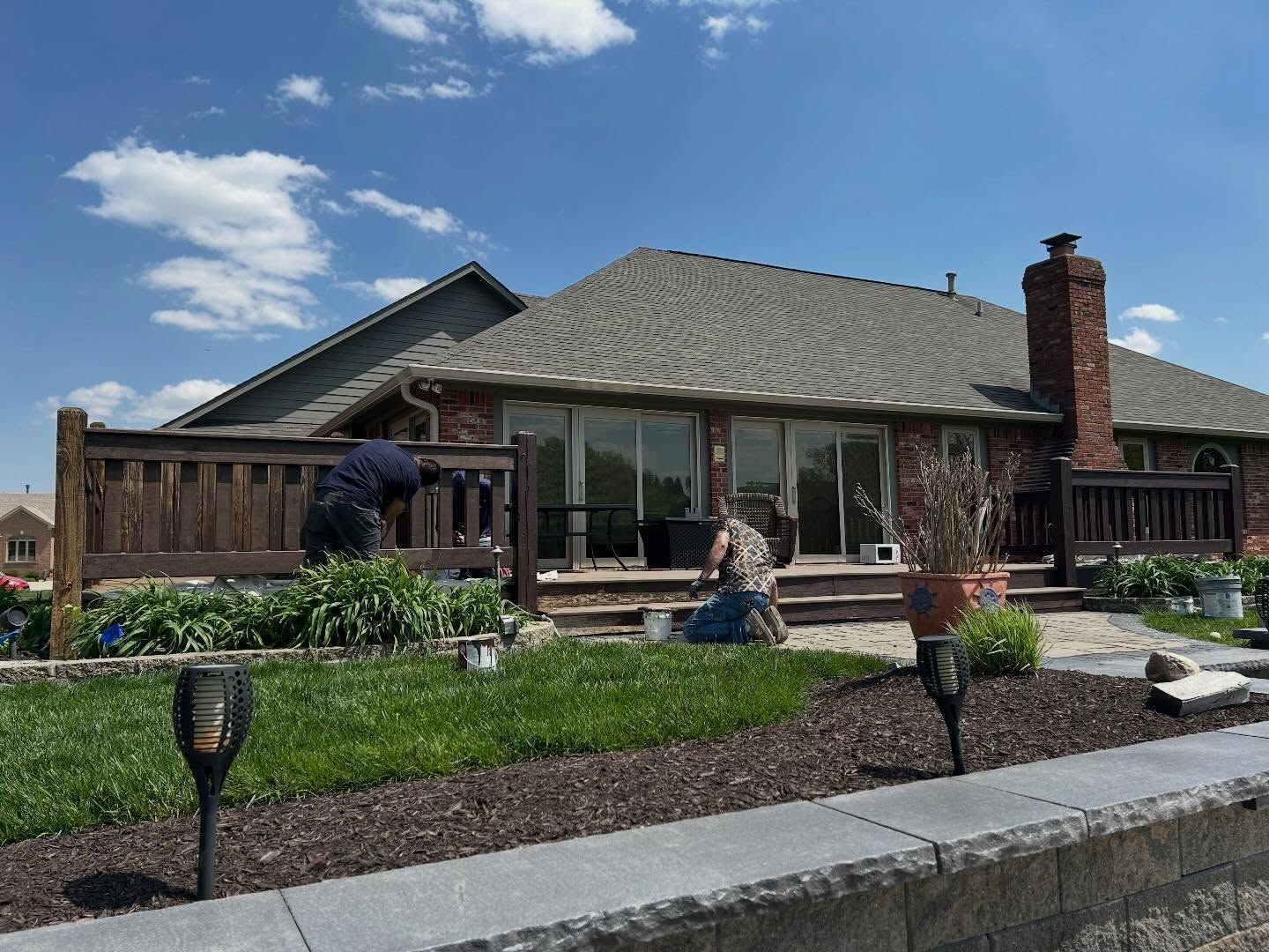Single-story house with a gray roof, brick chimney, and landscaped front yard under a blue sky