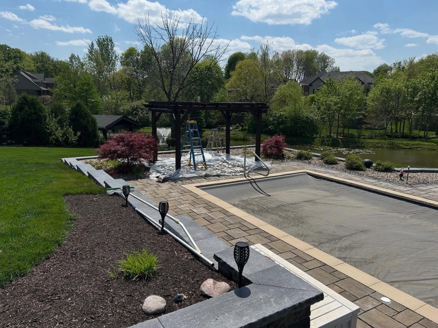 Backyard patio with pergola, stone path, lawn, shrubs, and a concrete pool under construction