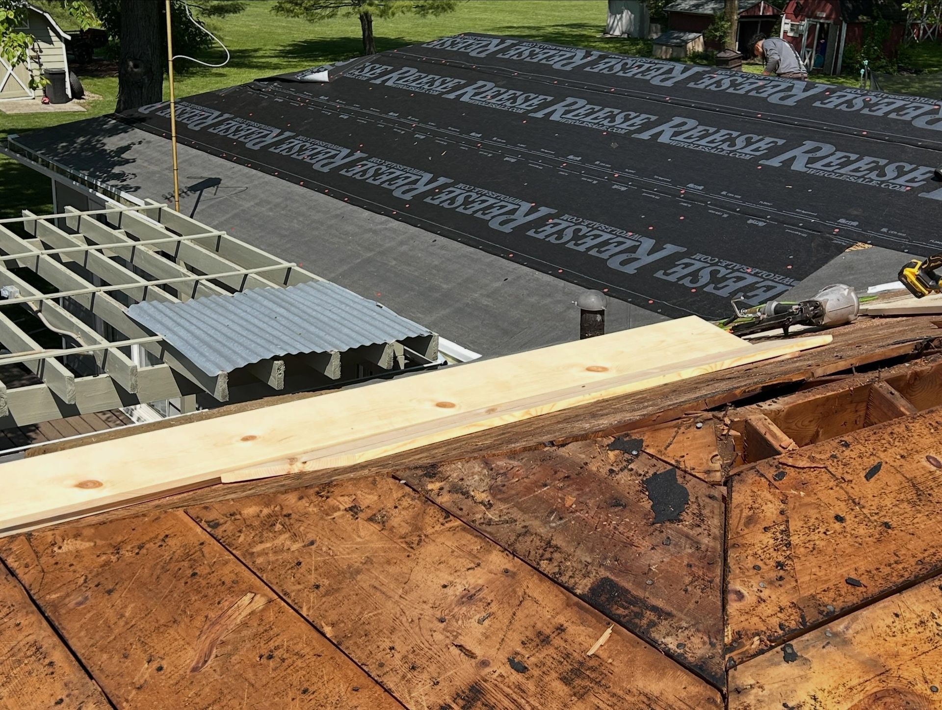 Roof under construction next to a road, green trees, and a small parking area below.