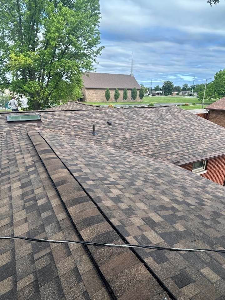 Residential rooftops with brown shingles beside a tree under a cloudy sky