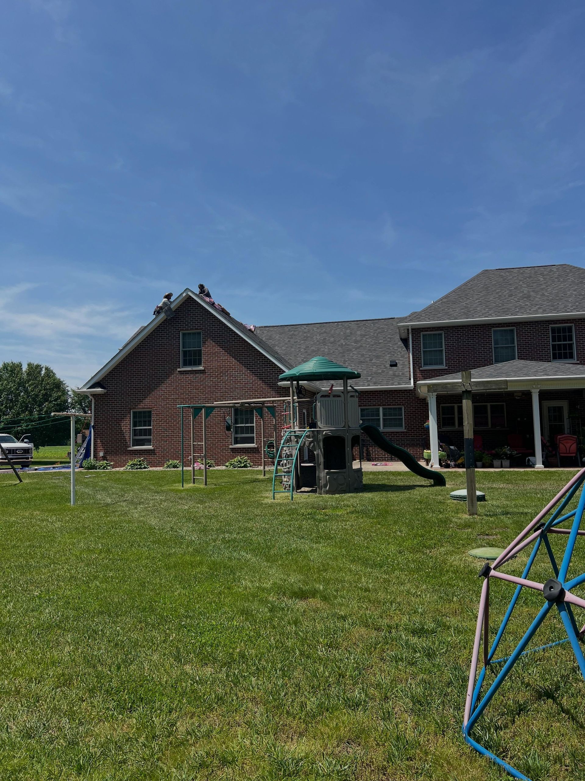 Red brick house with lawn, playground climbing dome, and bright blue sky