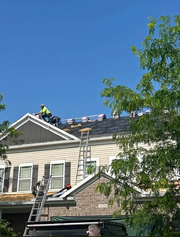 Workers repairing a roof on a beige house under a clear blue sky