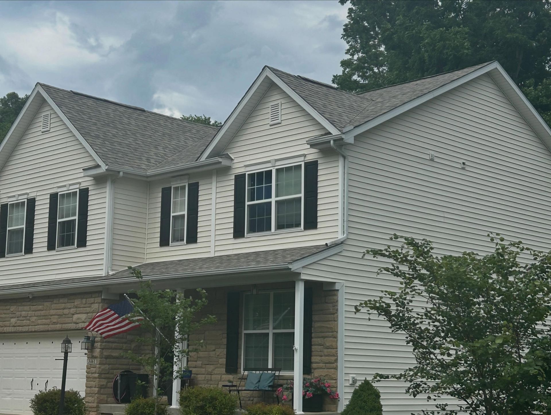 Suburban two-story house with white siding, black shutters, and an American flag by the front door