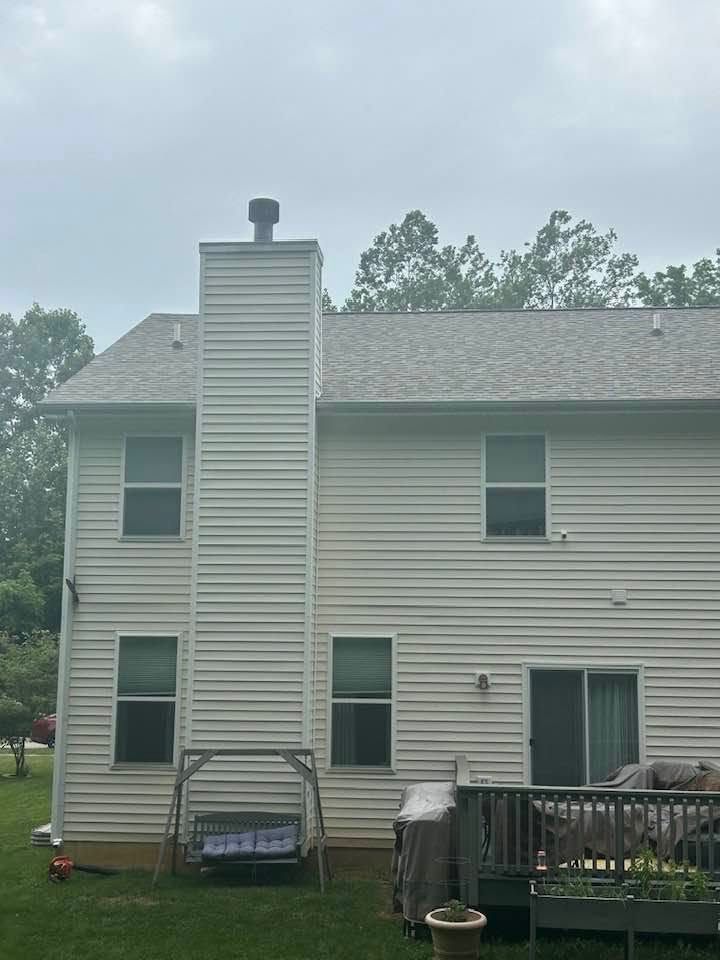 Two-story beige house with deck, chimney, and backyard swing set under a cloudy sky