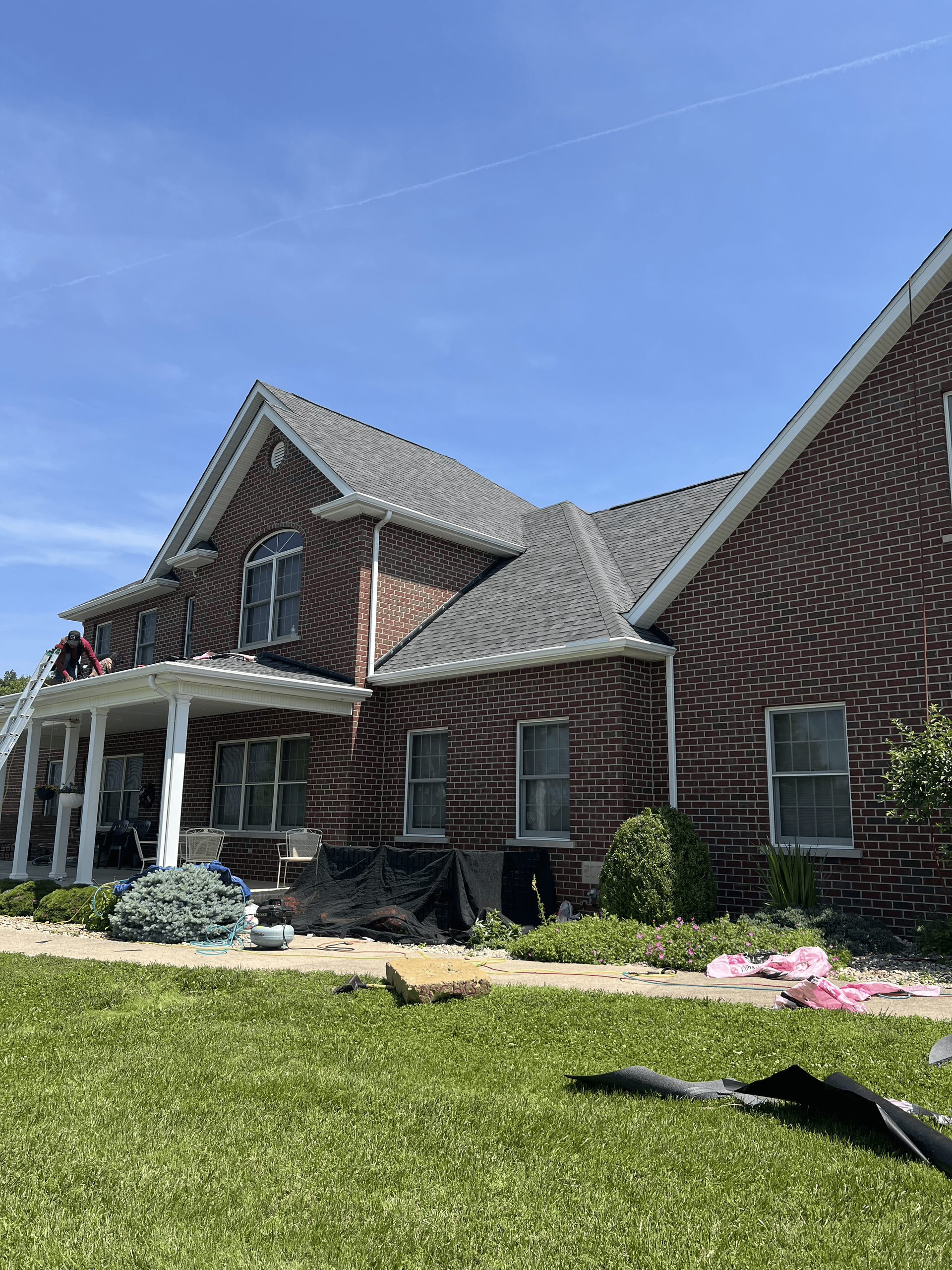 Brick house with white porch columns and gray roof under a clear blue sky