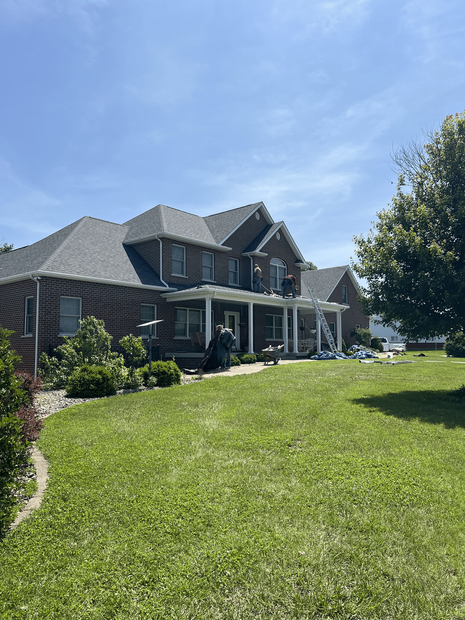 Large gray house with a steep roof and front porch beside a bright green lawn under a blue sky