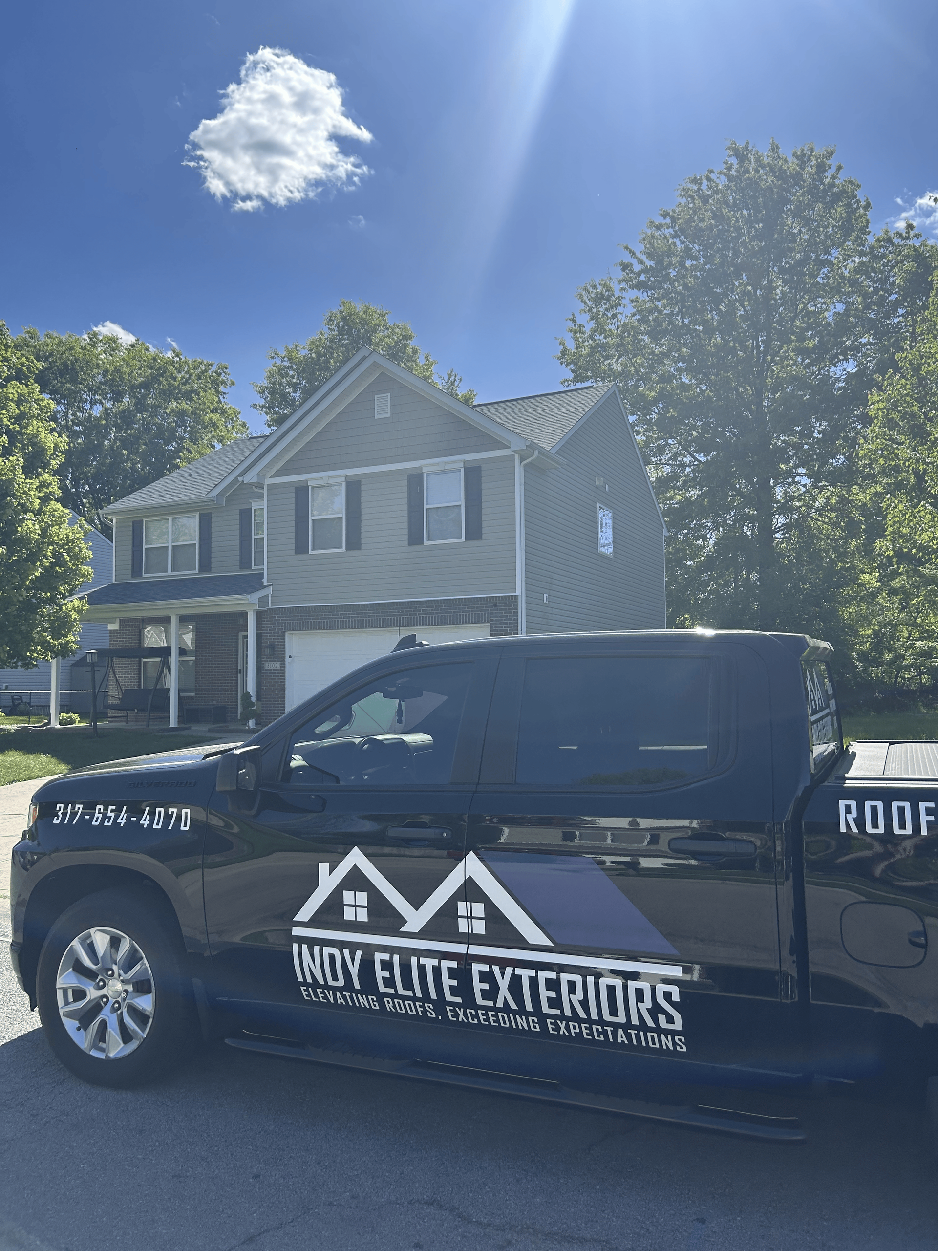 Black pickup with Indy Elite Exteriors logo parked in front of a gray house on a sunny day