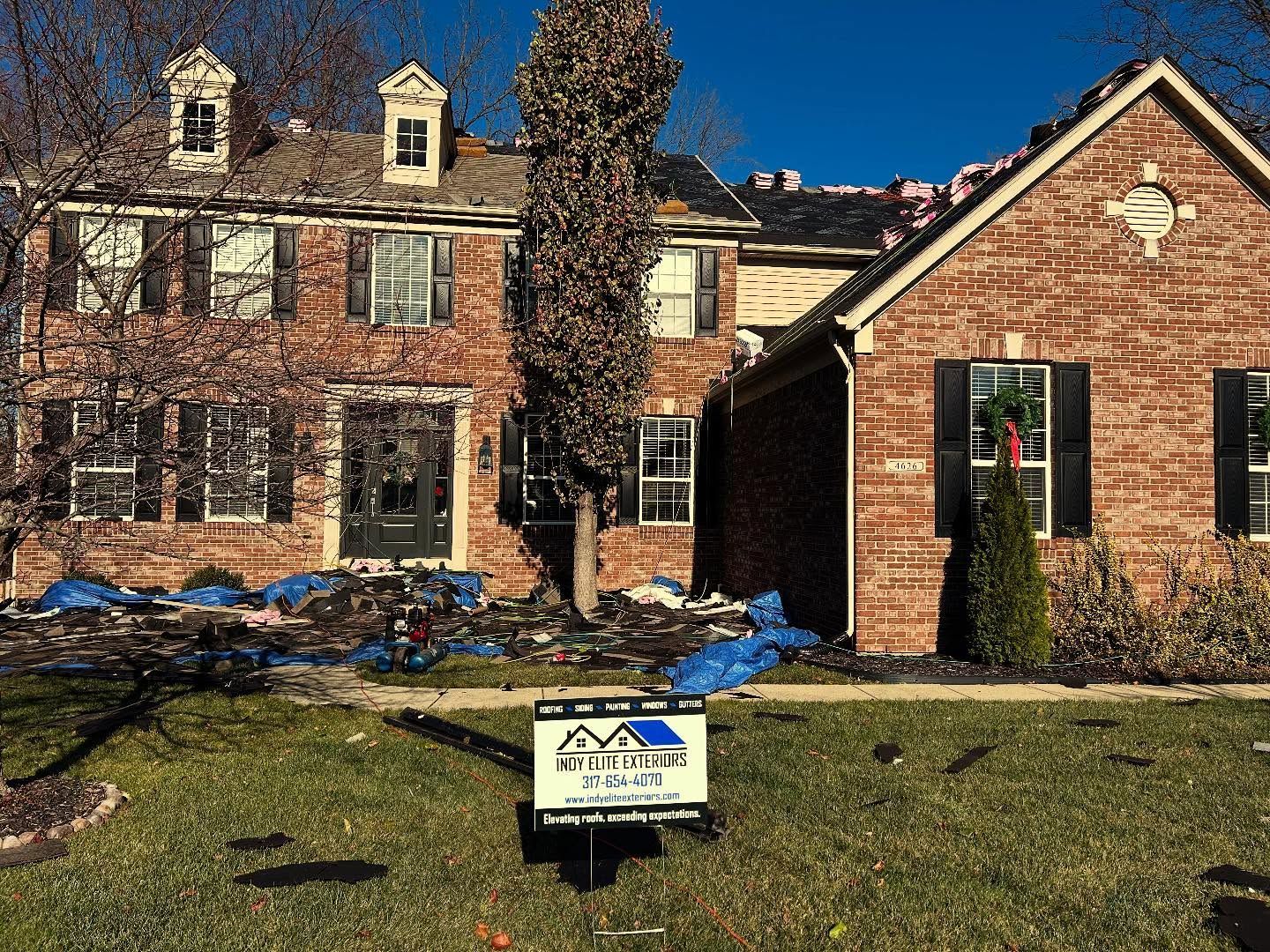 Brick house undergoing roof work with an Indy Elite Exteriors sign in the front yard