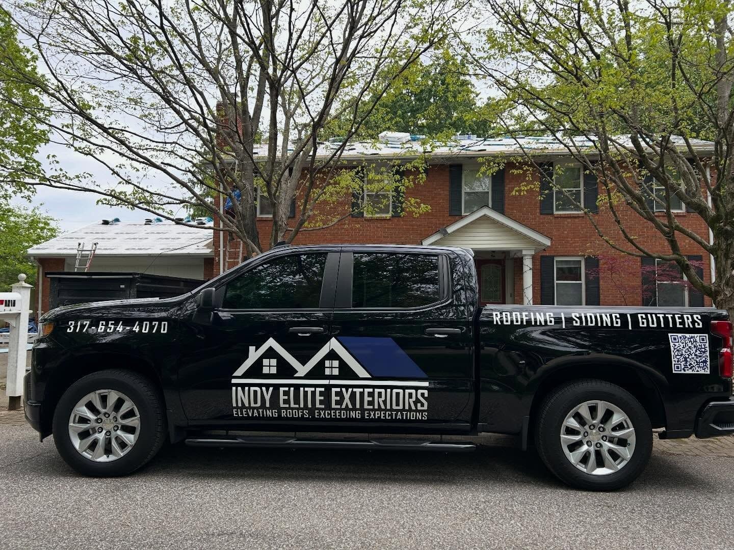 Black Indy Elite Exteriors pickup truck parked in front of a brick house with trees.