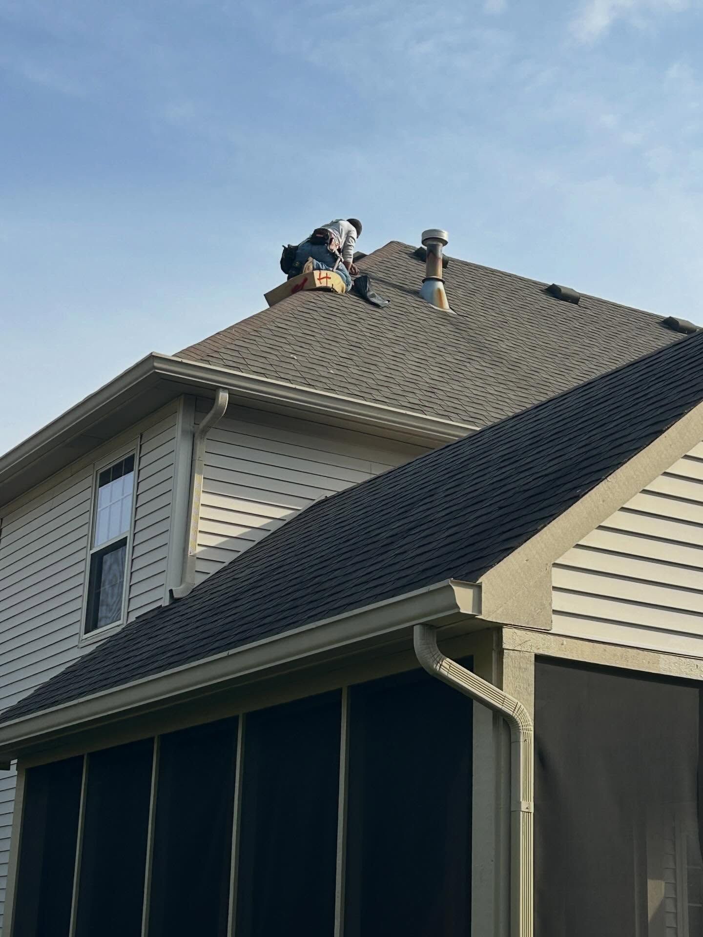 A roofer working on a gray shingled house roof under a blue sky
