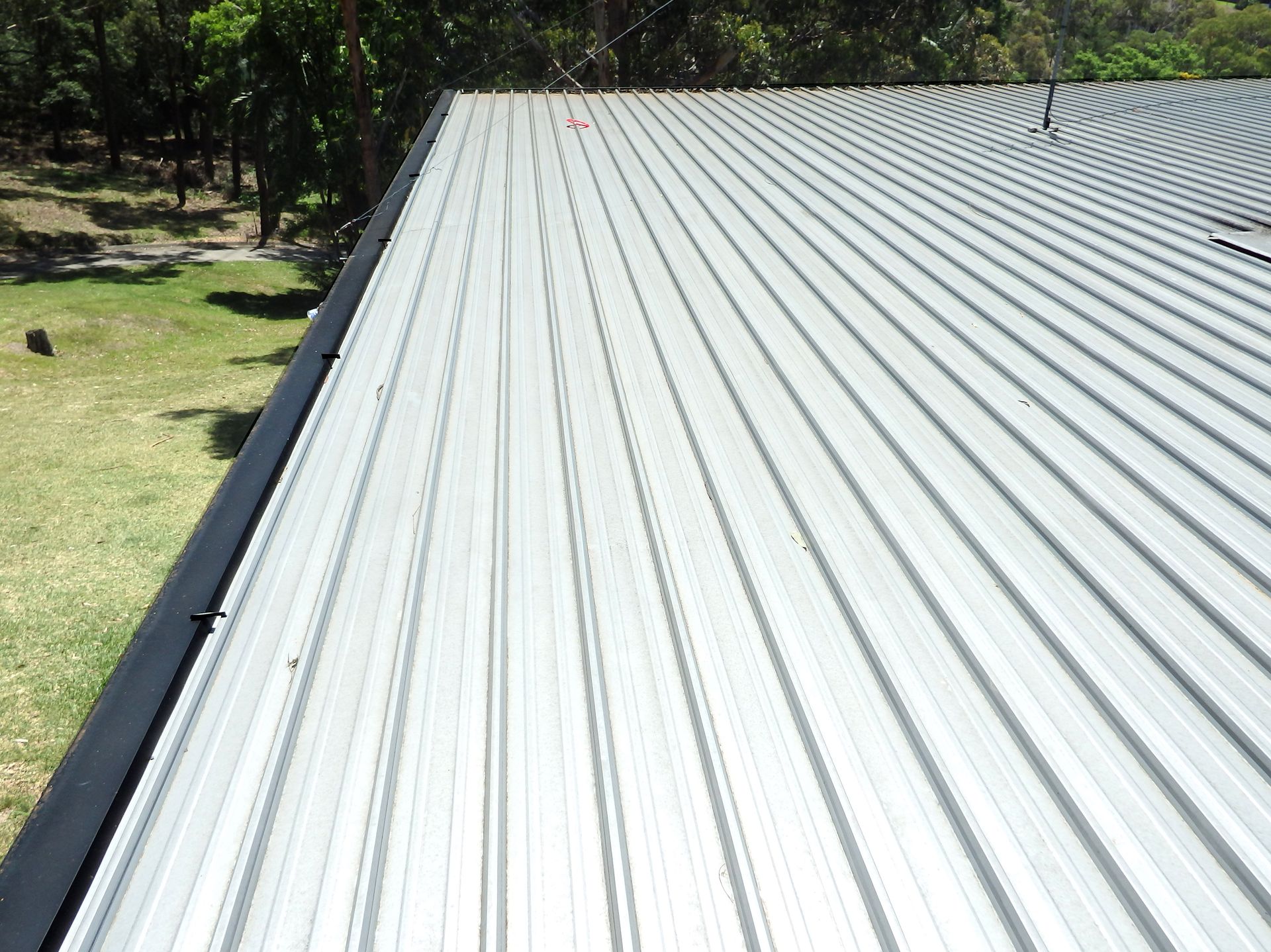Corrugated metal roof stretching into the distance beside a grassy yard and trees