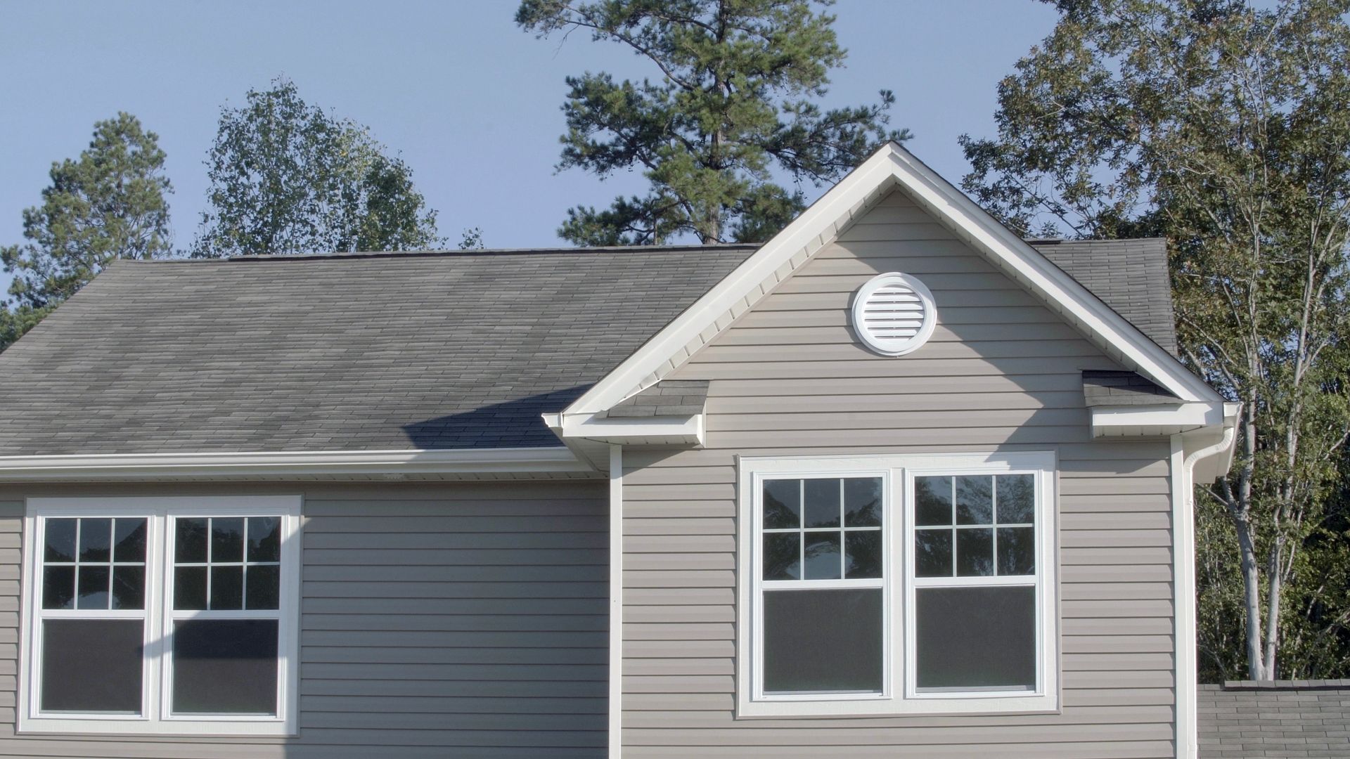 Gray house exterior with white trim and gabled roof under trees
