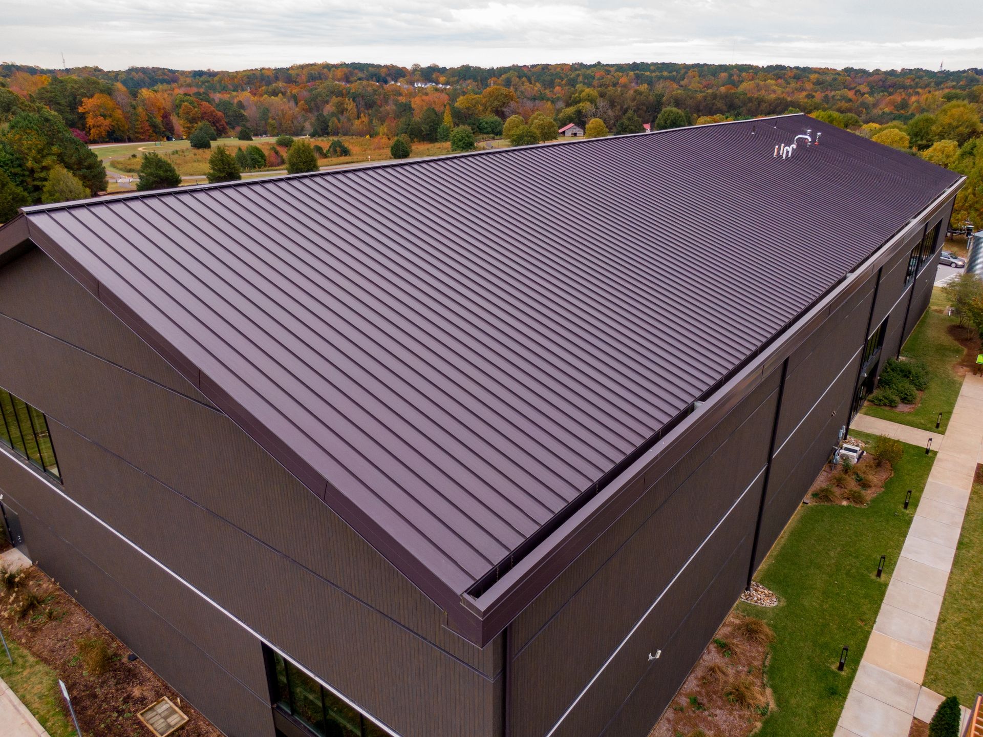 Aerial view of a large brown building with a dark metal roof surrounded by trees and grass