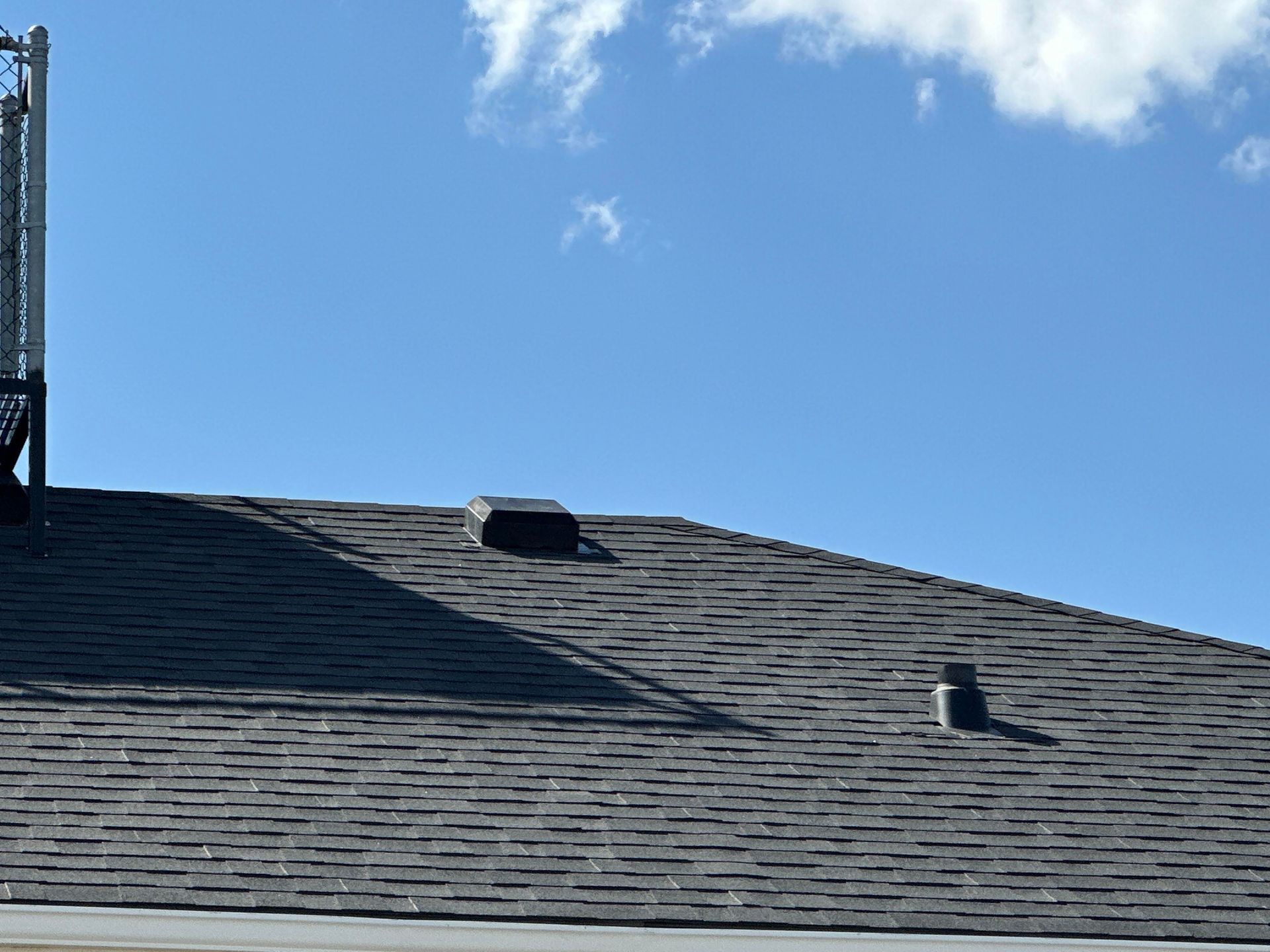 Blue sky above a gray shingled roof with two roof vents and a small cloud