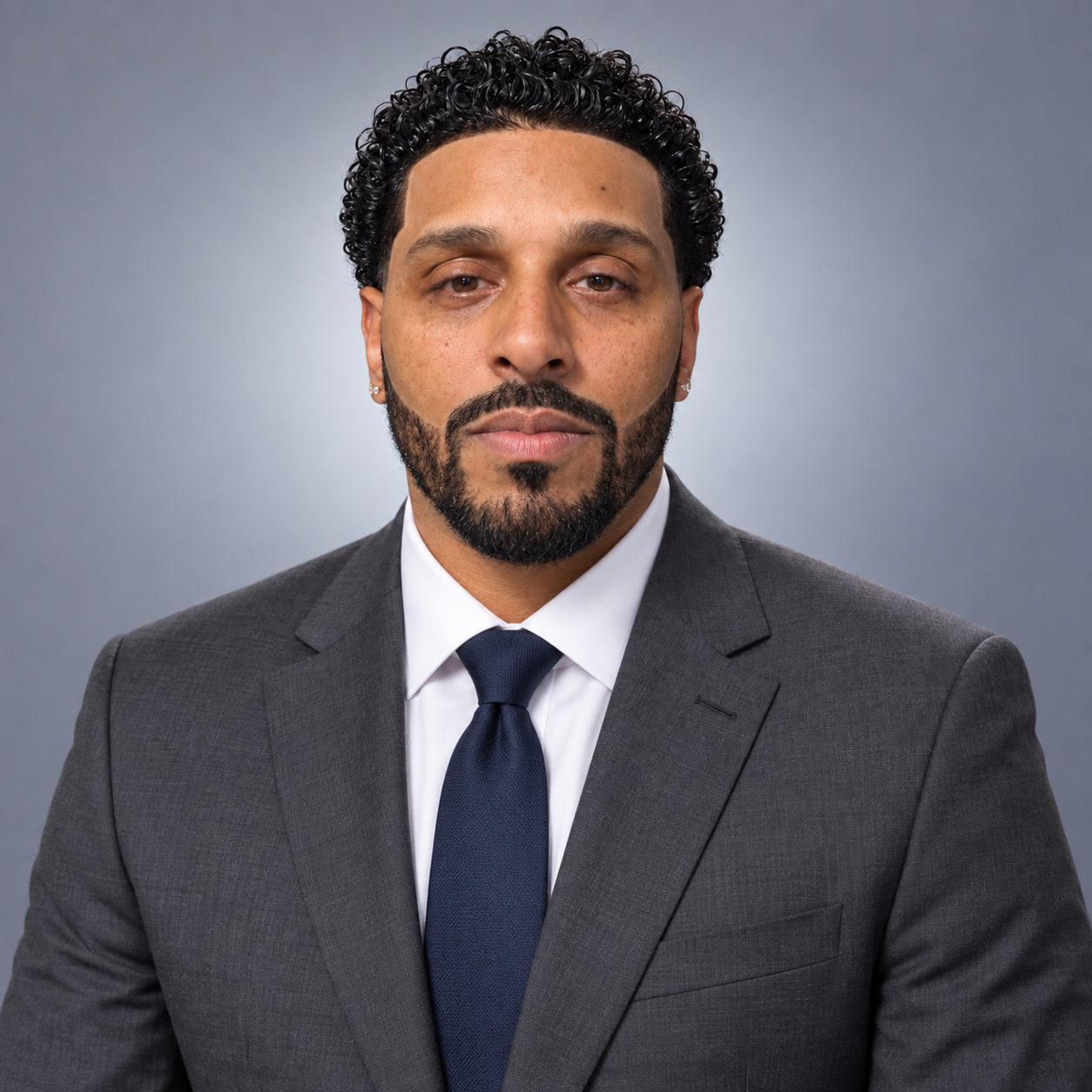 Man in a dark gray suit, white shirt, and navy tie against a gray studio background