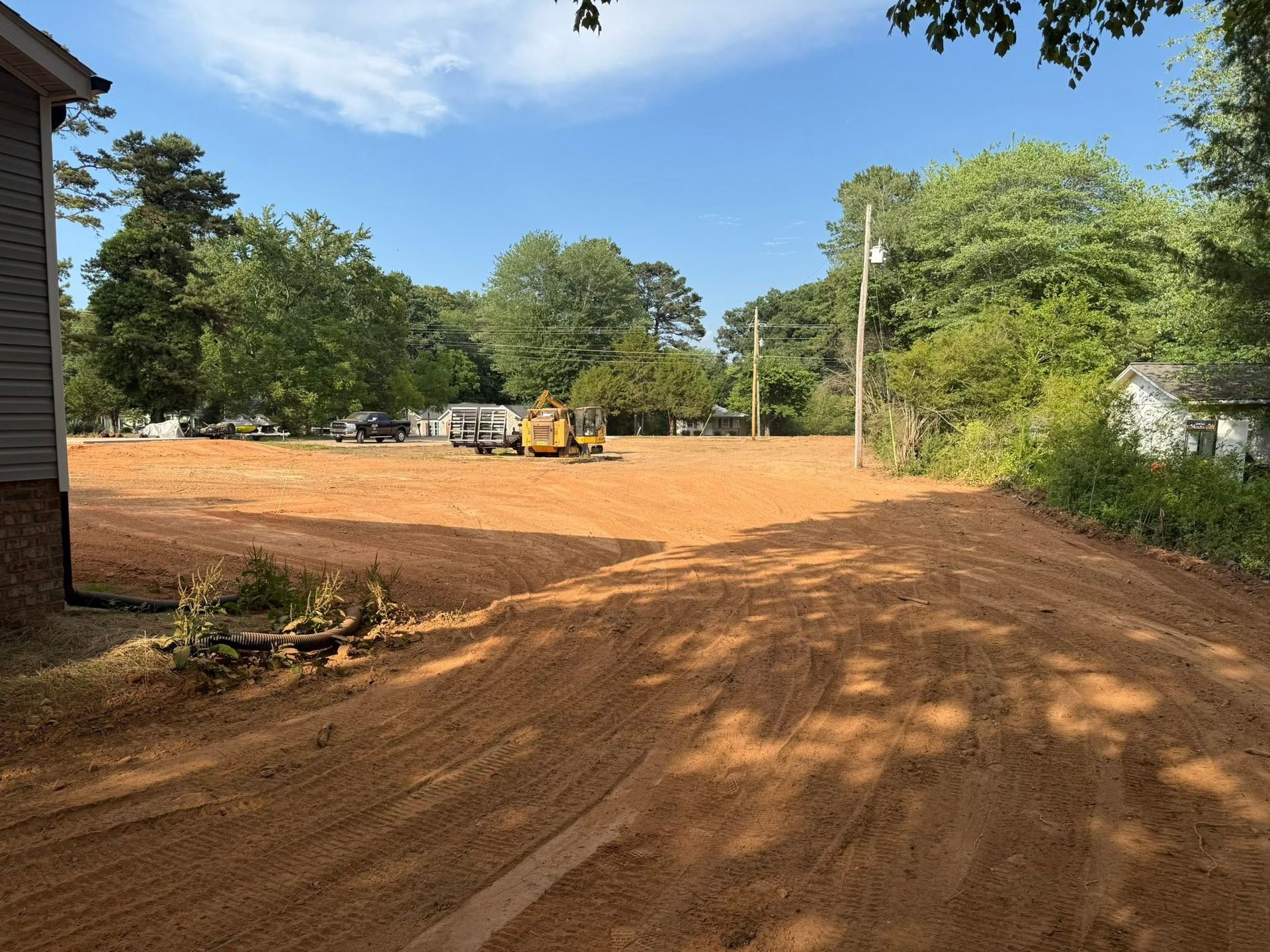Cleared dirt lot with construction equipment, trees, and a blue sky