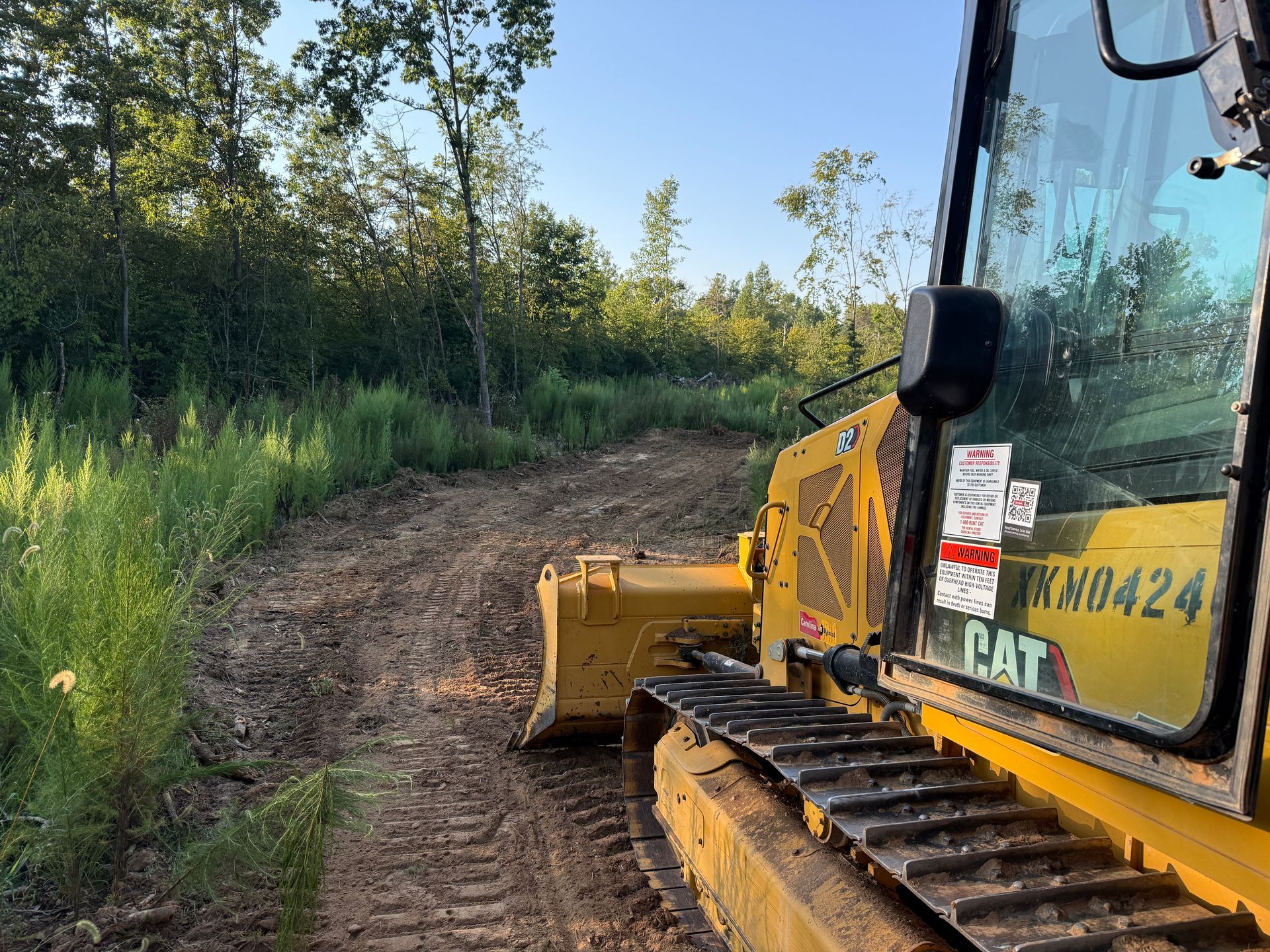Yellow CAT bulldozer on a muddy dirt path beside tall green trees