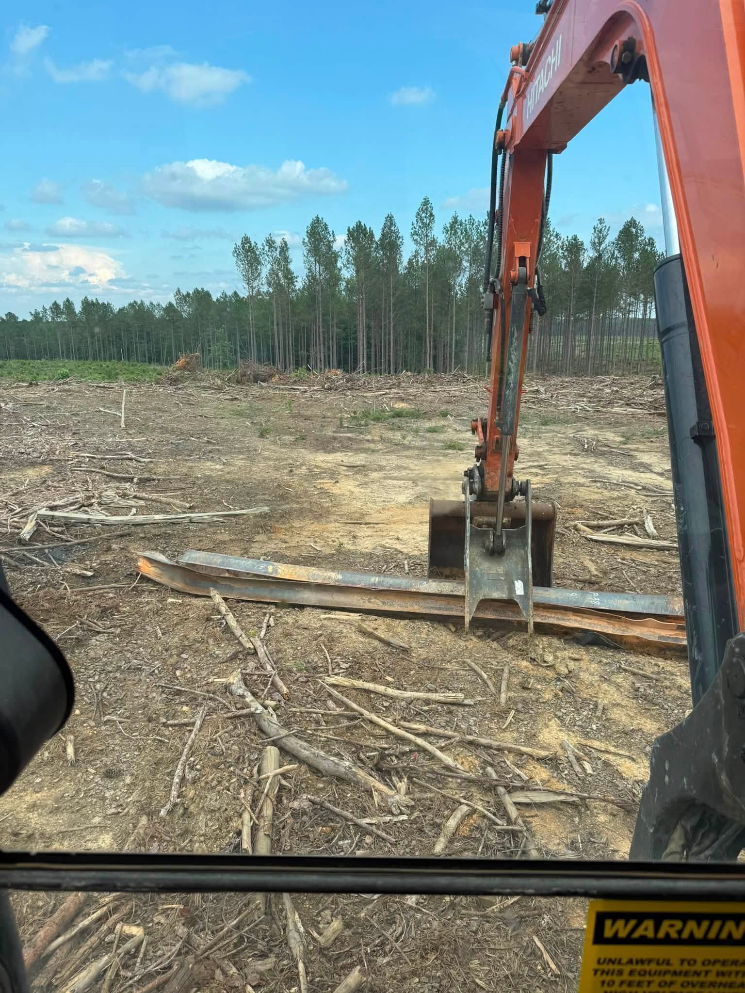 Excavator bucket clearing brush on a logged forest site under a blue sky