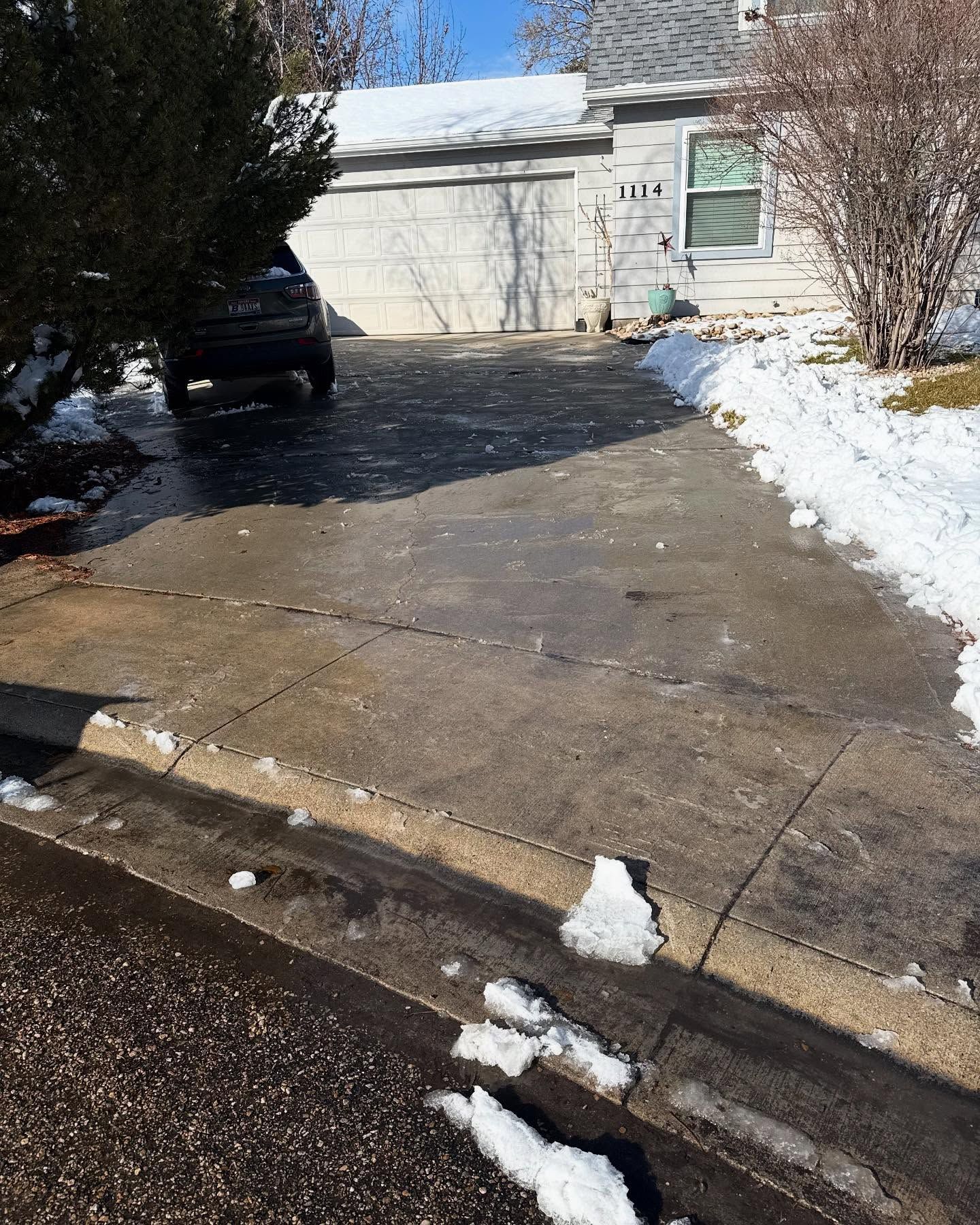 Snowy driveway leading to a garage with a parked black car and patches of snow along the curb