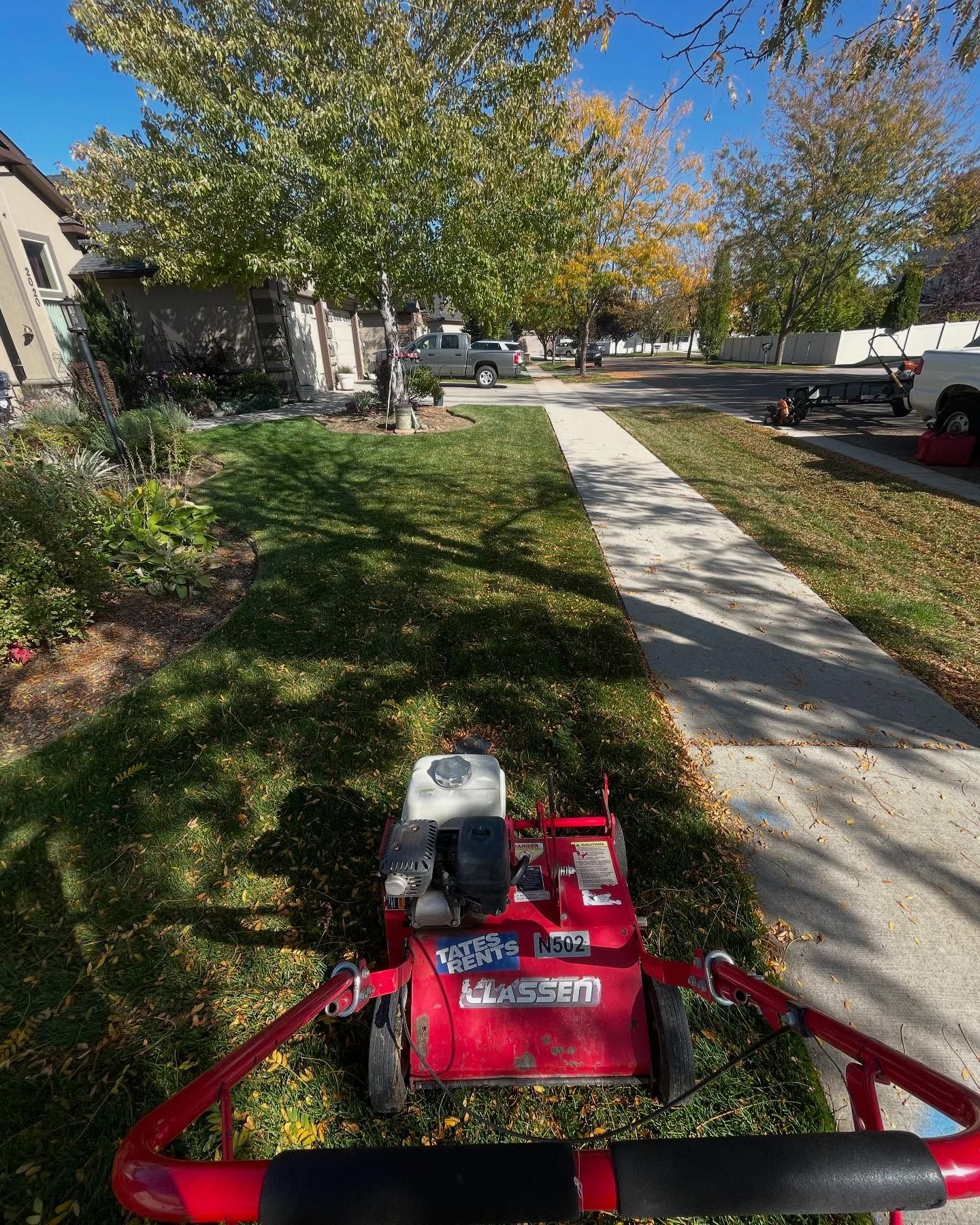 Lawn mower on a suburban sidewalk beside houses and trees on a sunny day