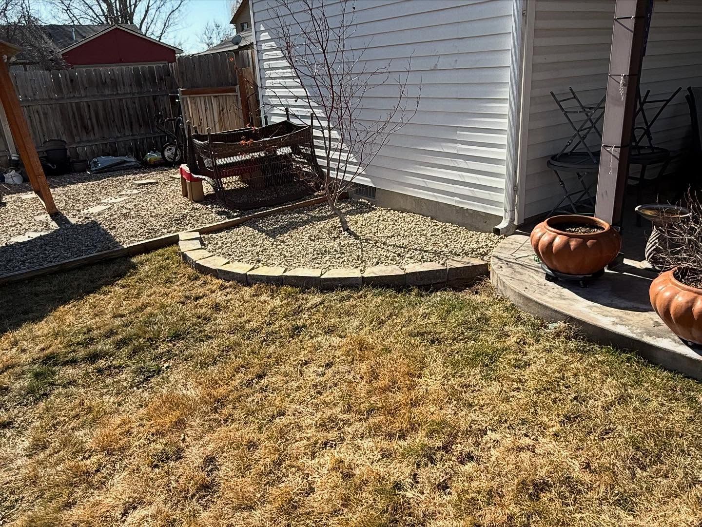 Backyard with patchy grass, white house siding, a covered bench, and two orange pots by the wall.