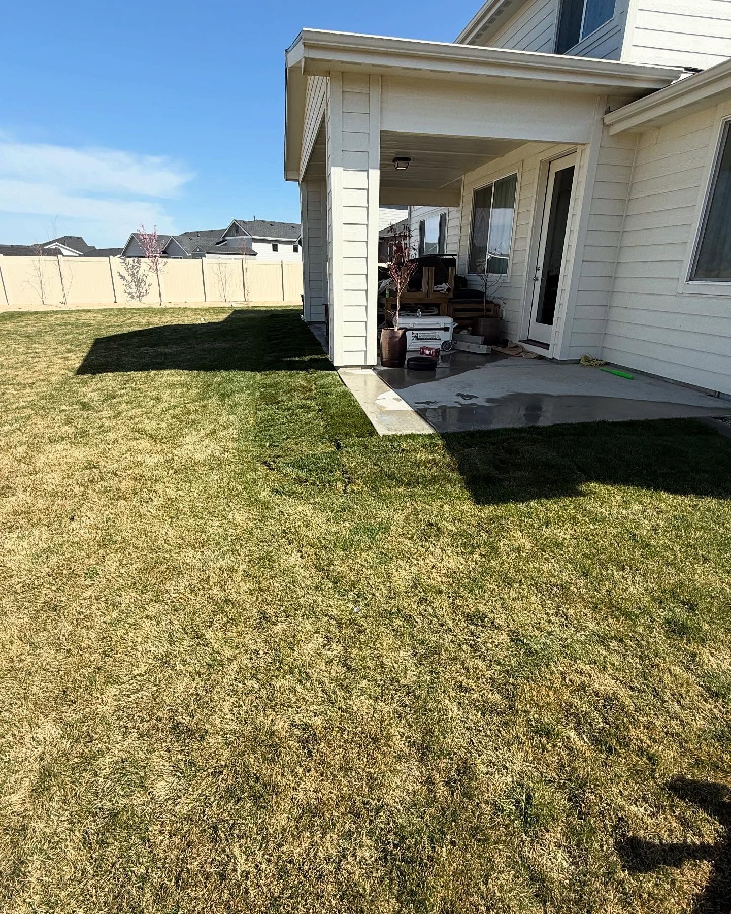 Suburban backyard with a grassy lawn and a covered patio attached to a white house.