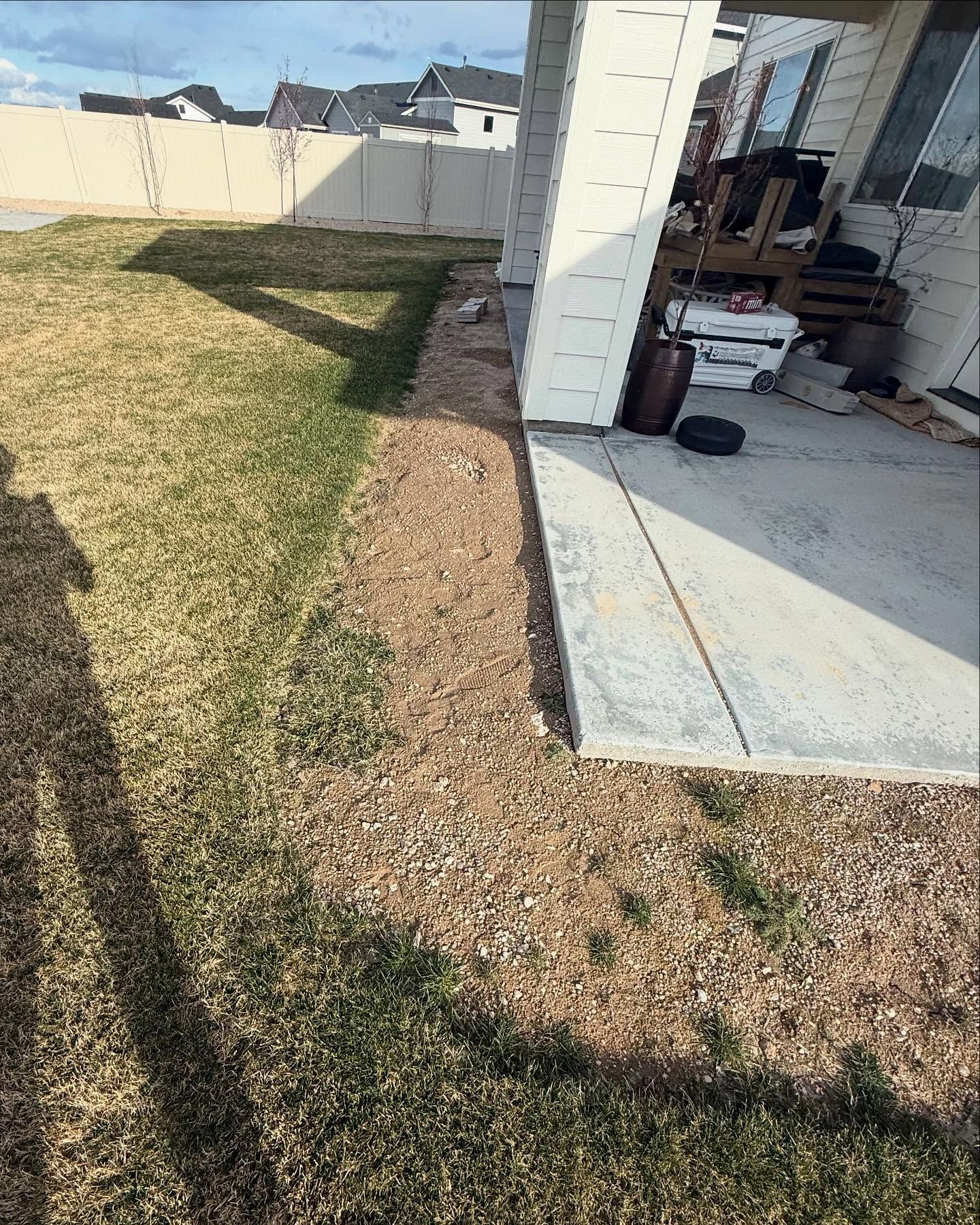Backyard with dry grass beside a house patio and a narrow gravel border along the wall