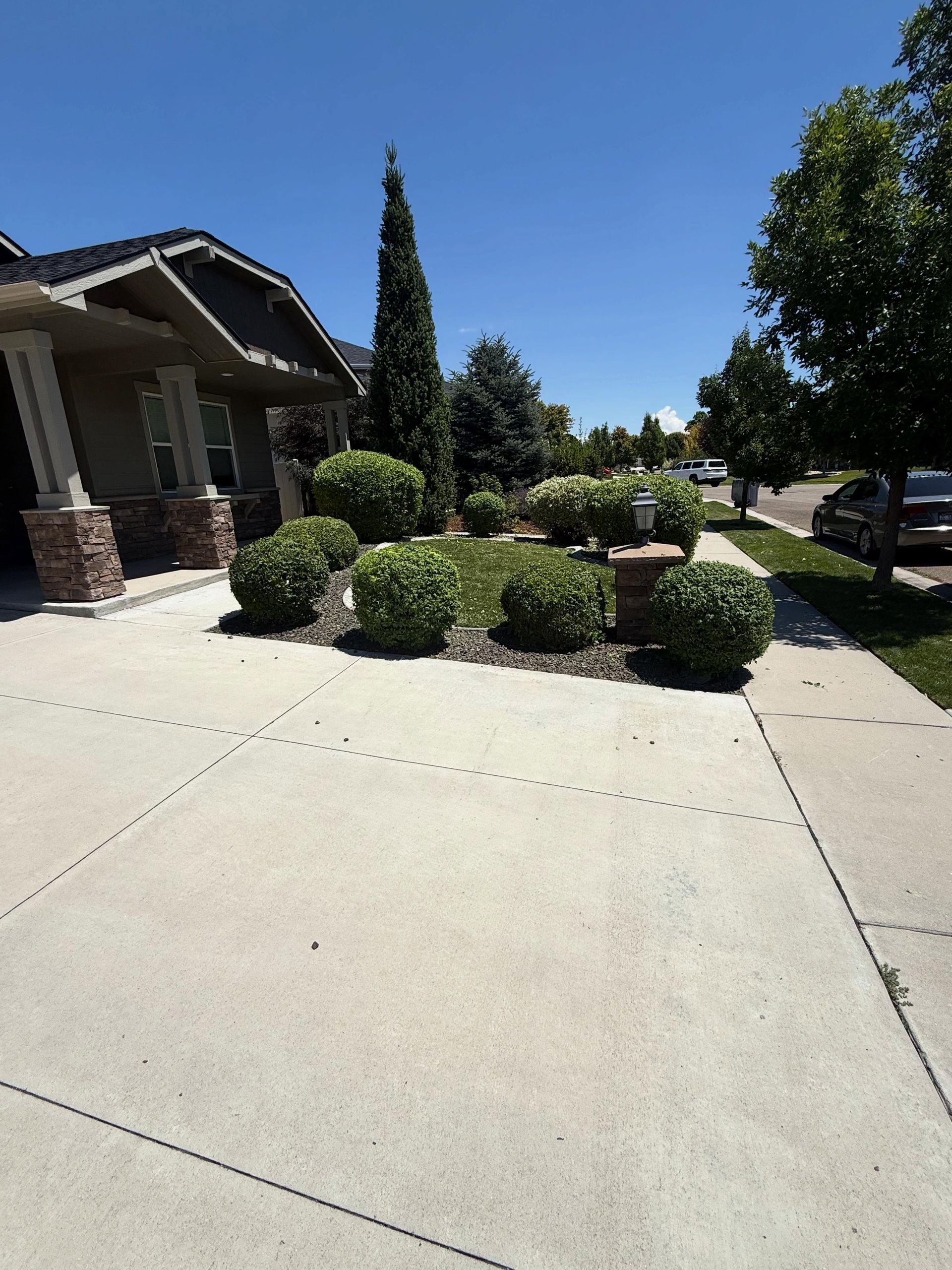 Suburban home entrance with a wide driveway, landscaped shrubs, and a clear blue sky.