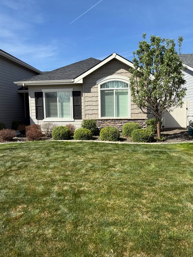 Single-story beige house with white trim, front lawn, shrubs, and a blue sky backdrop
