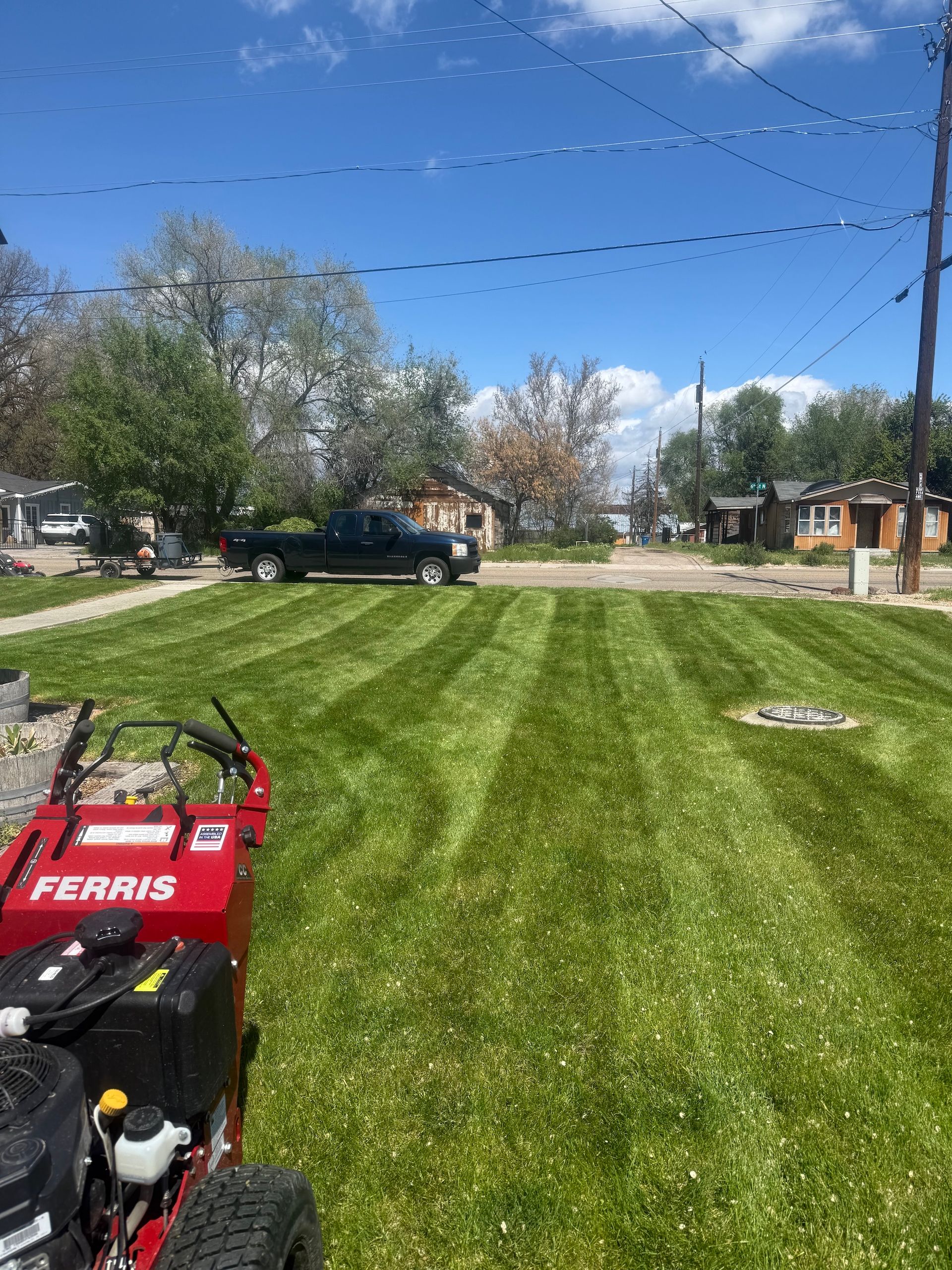 Freshly mowed lawn with striped grass, a red Ferris mower in front, and a truck on a residential street.