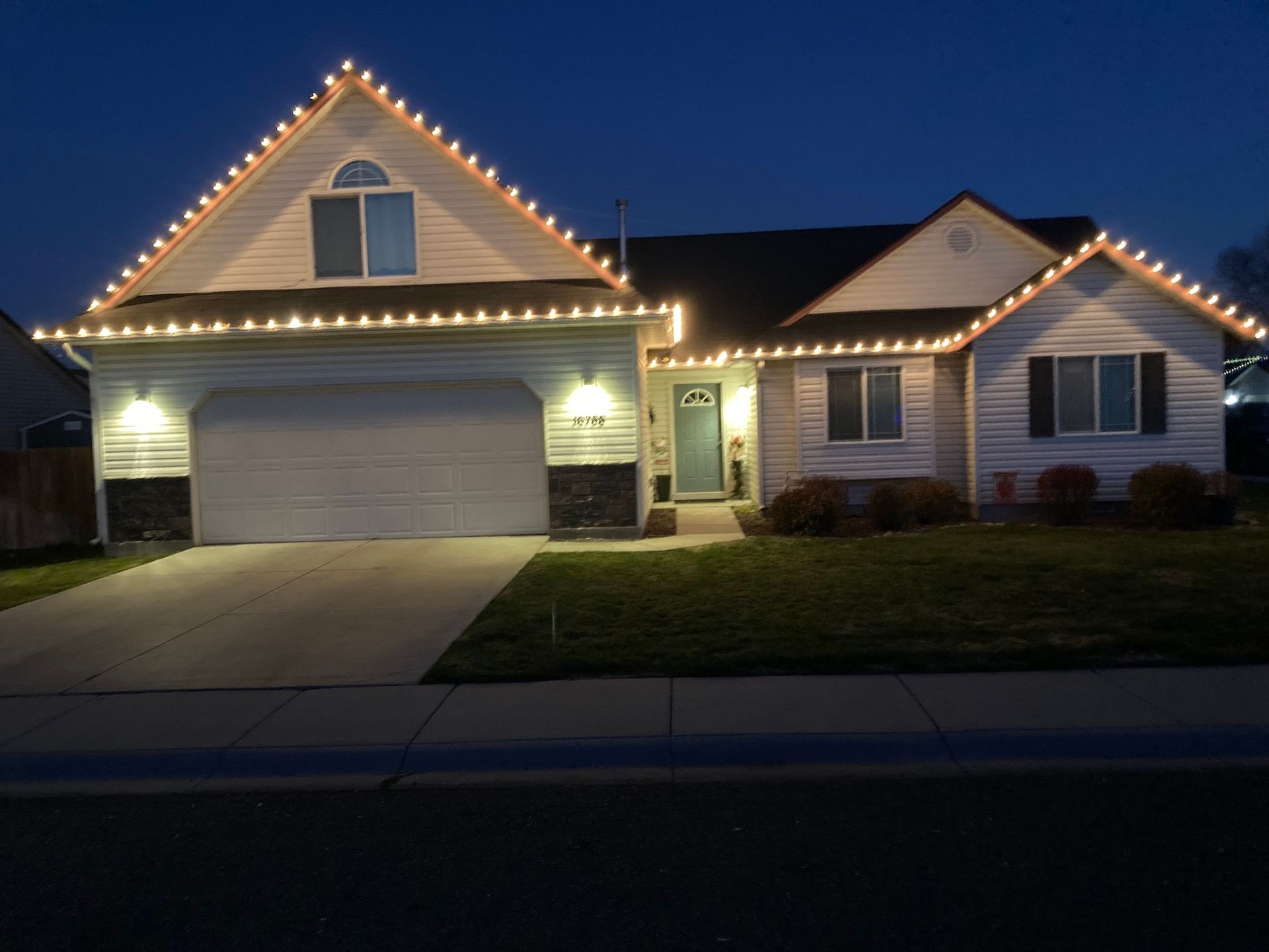 Suburban house at dusk with garage, porch lights, and roofline Christmas lights illuminated