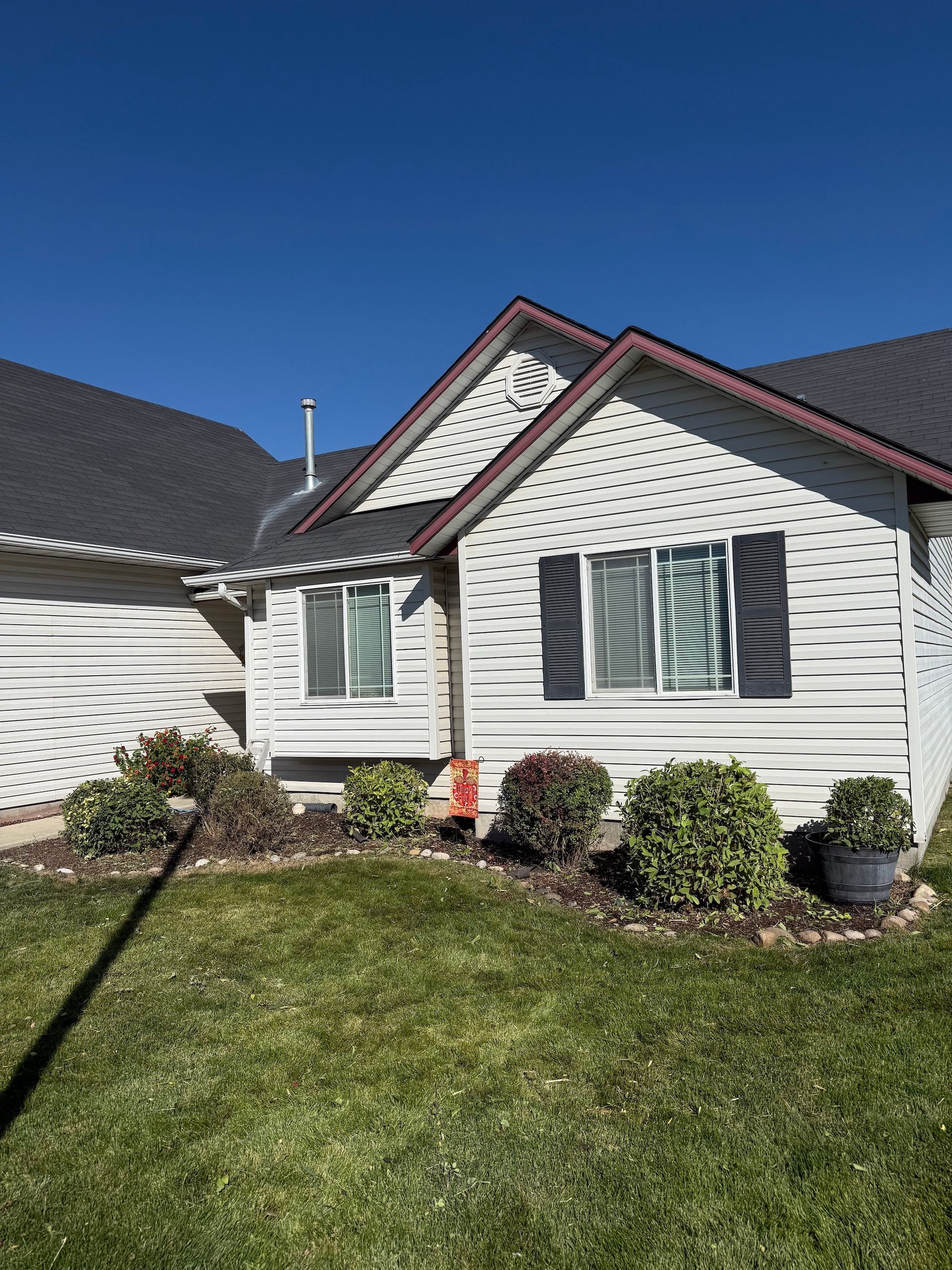 White suburban house with green shutters, red trim, and a neat front lawn under a clear blue sky