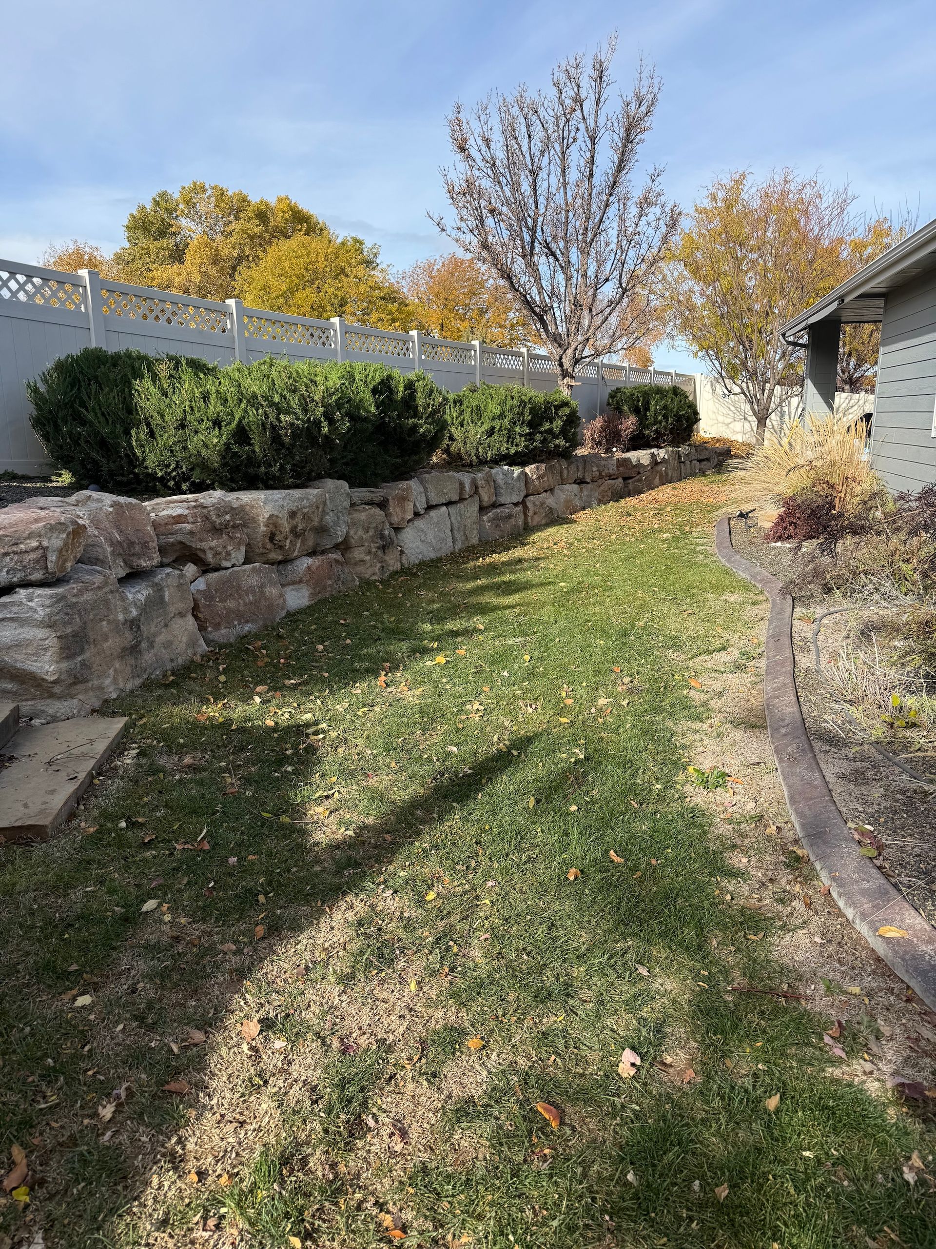 Stone garden path between retaining walls and shrubs under autumn trees, beside a house
