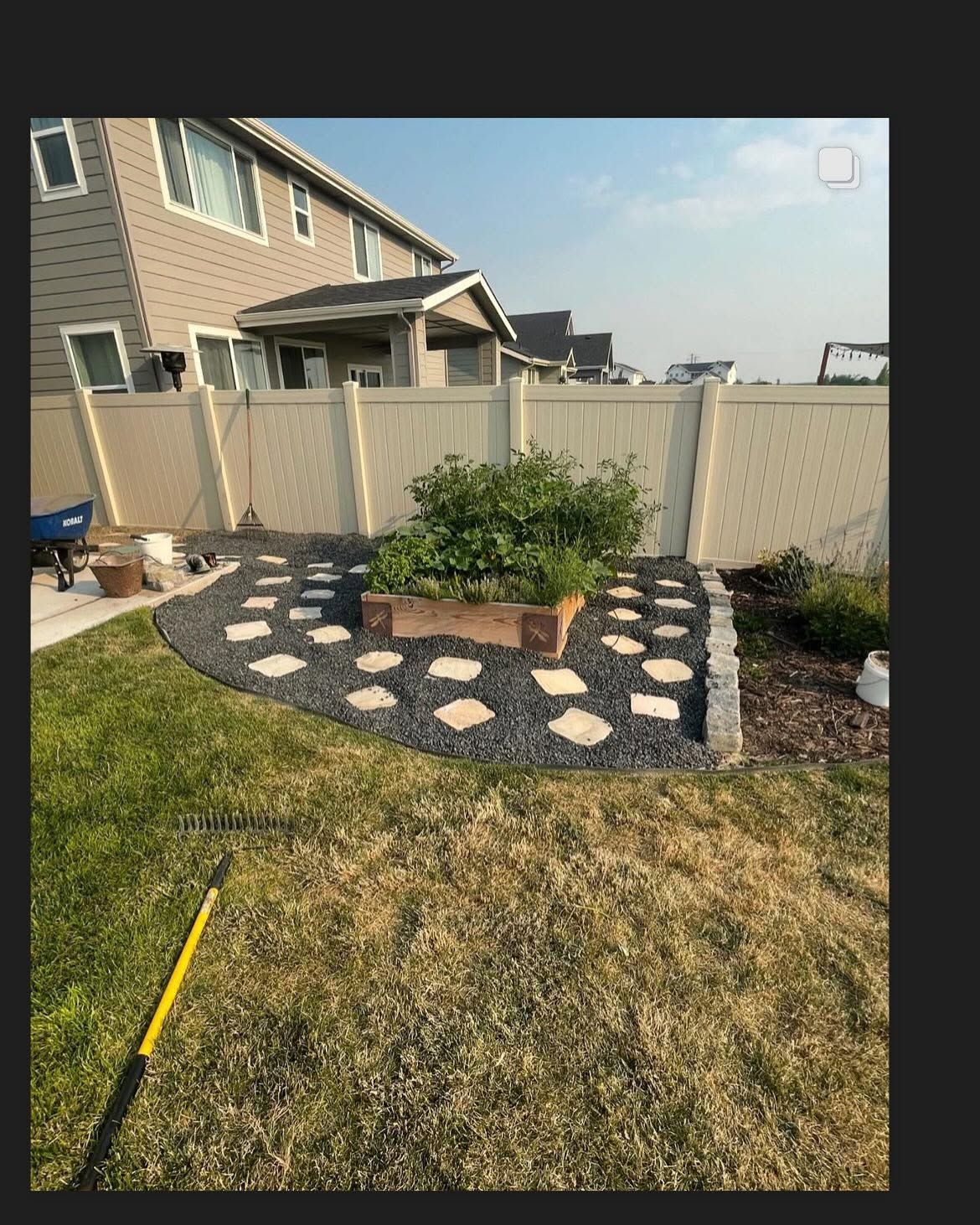 Backyard garden bed with stepping stones, shrubs, and a wooden fence beside a house