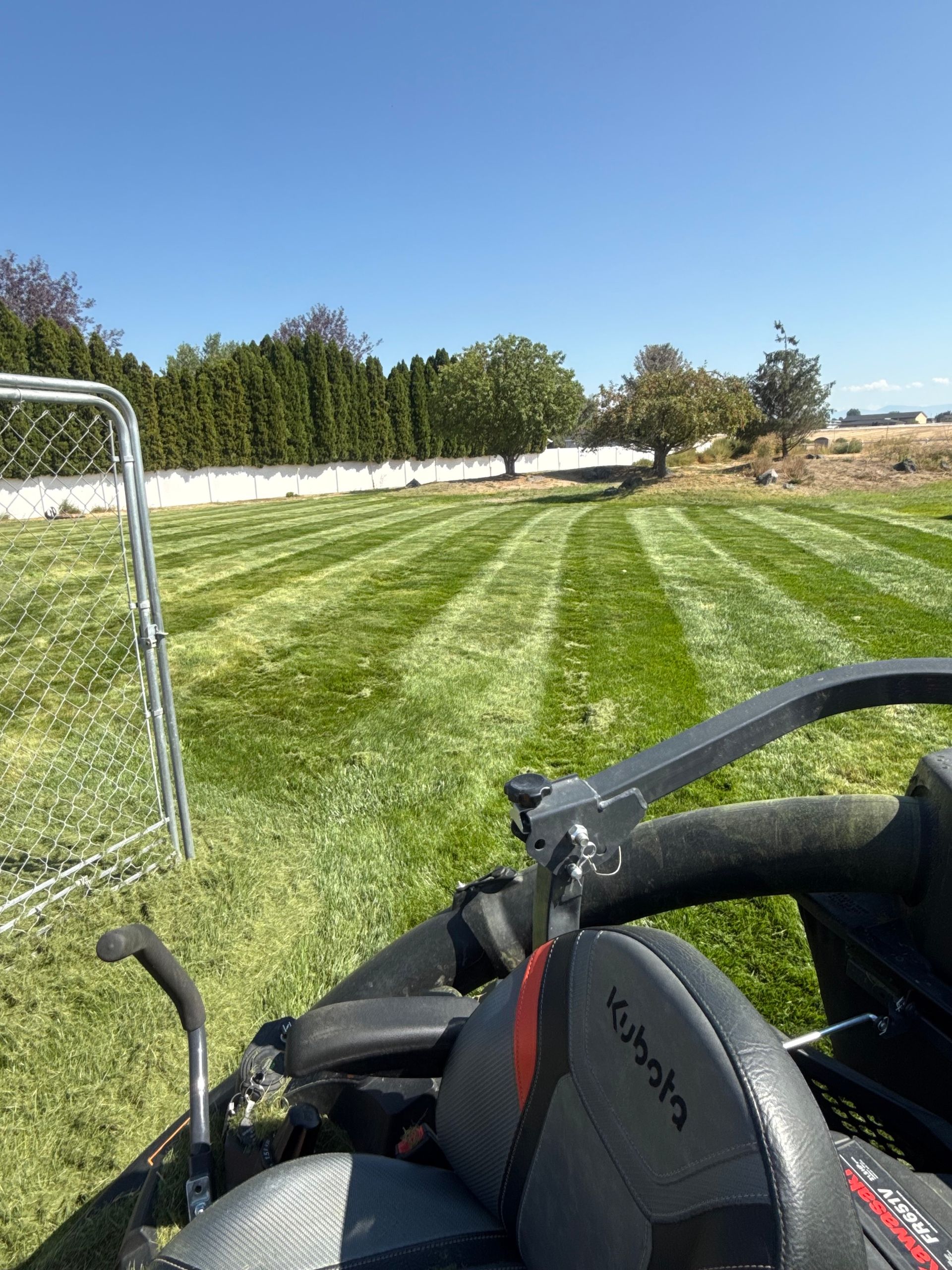 Lawn striped by mower, with a blue sky and a golf cart handle in the foreground
