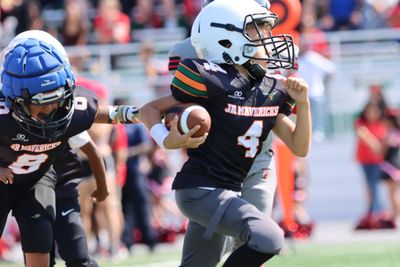 Football player in silver uniform runs with ball on a green field.